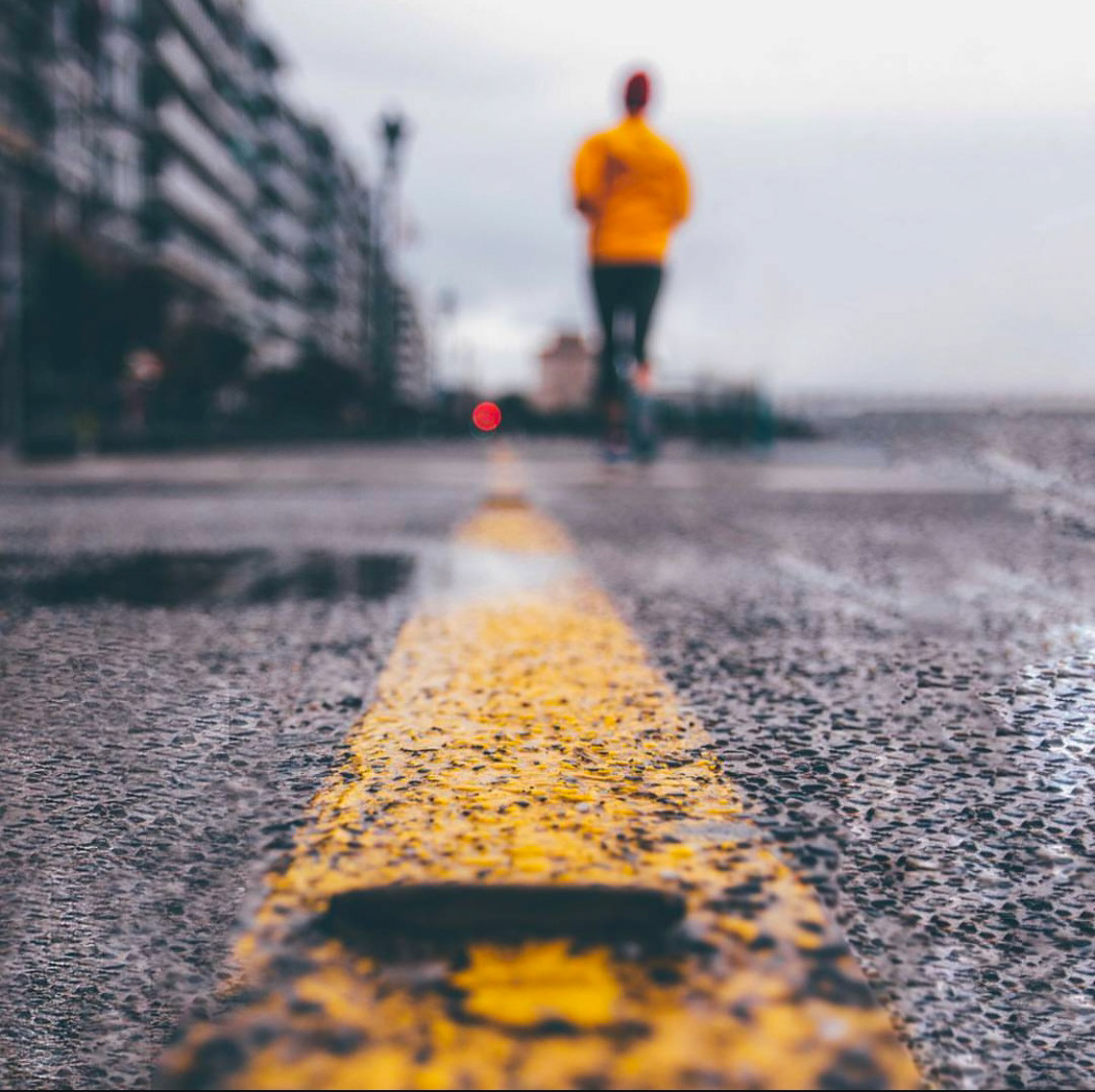 Close-up view of a yellow road marking with a blurred runner in yellow jogging in the background, highlighting motion and focus.