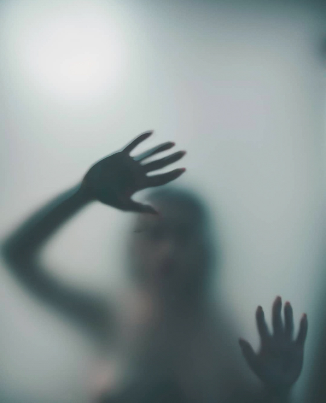 A blurred silhouette of a woman pressing her hands against a frosted glass, creating a mysterious and ethereal atmosphere.