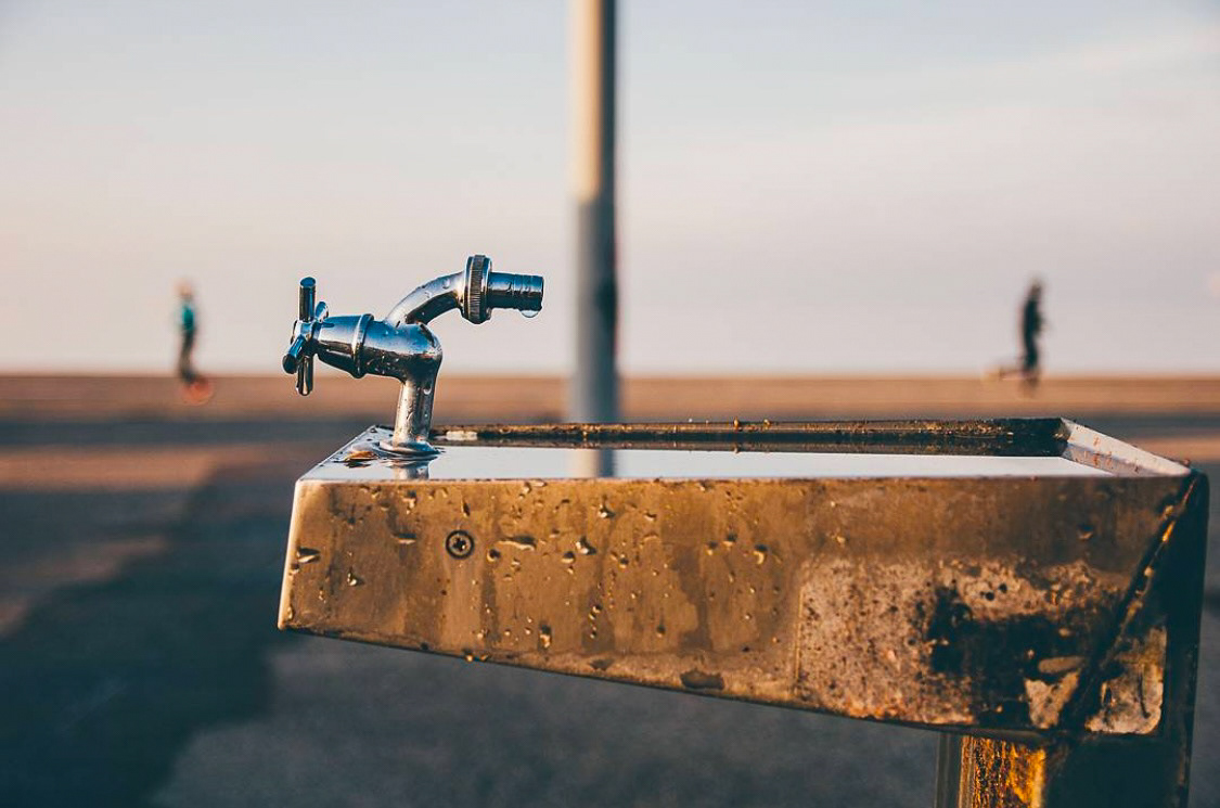 A rustic outdoor faucet with water droplets, blending industrial design with a backdrop of blurred activity.