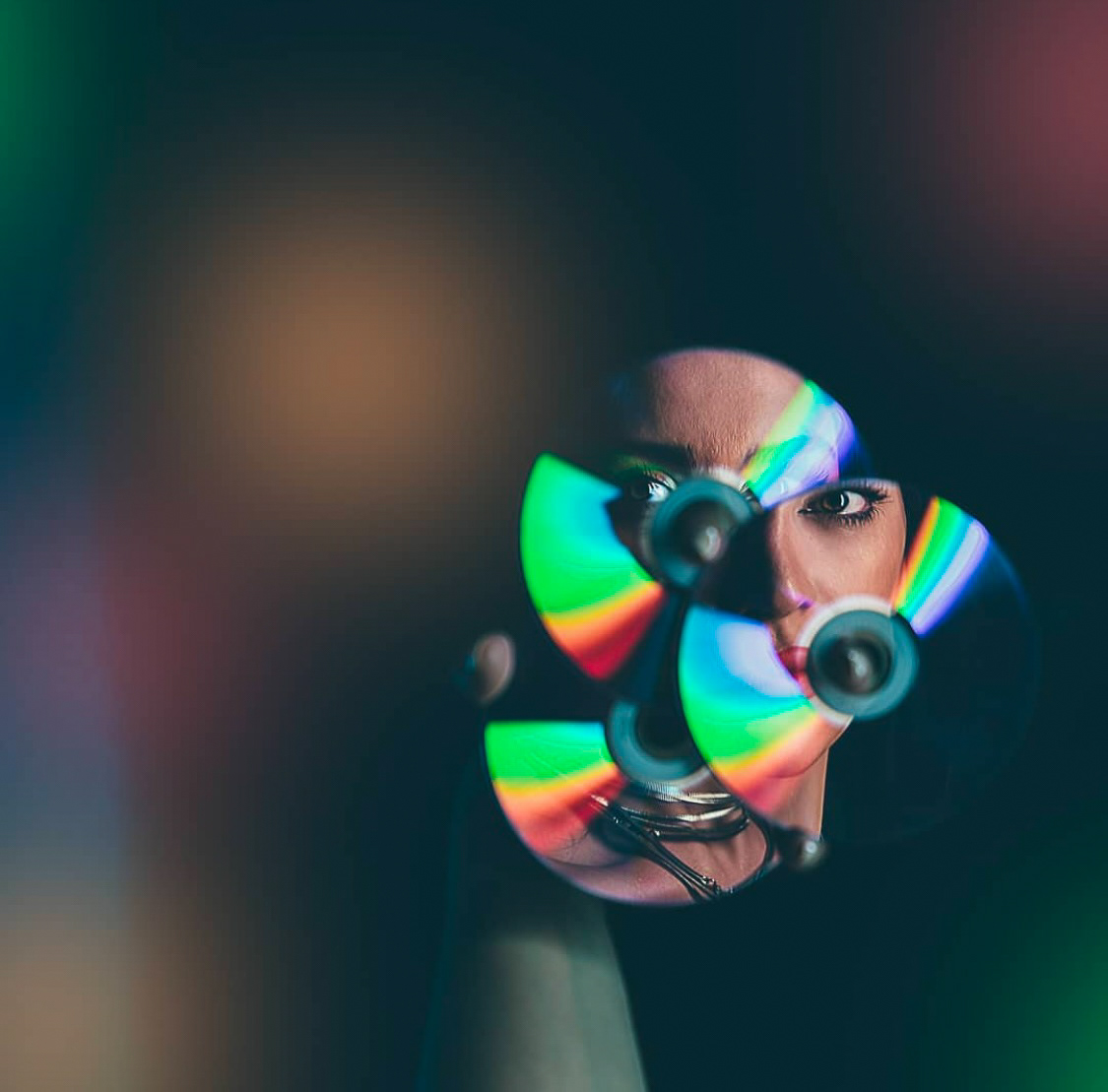 A creative portrait featuring a woman's face reflected through colorful CDs, showcasing a play of light and vibrant reflections