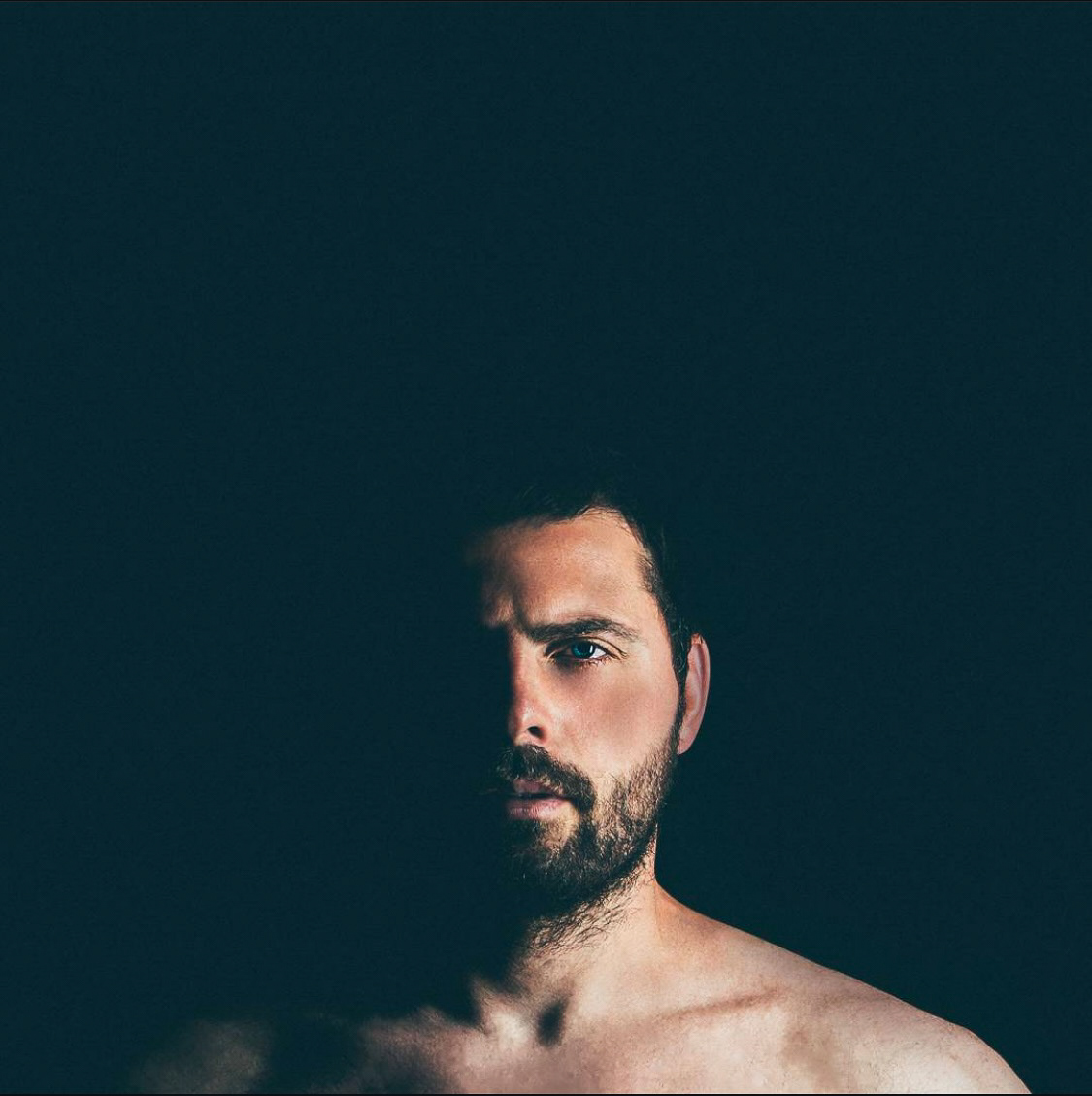 A portrait of a man partially illuminated in soft light, with intense shadows covering half his face, emphasizing depth and mystery.