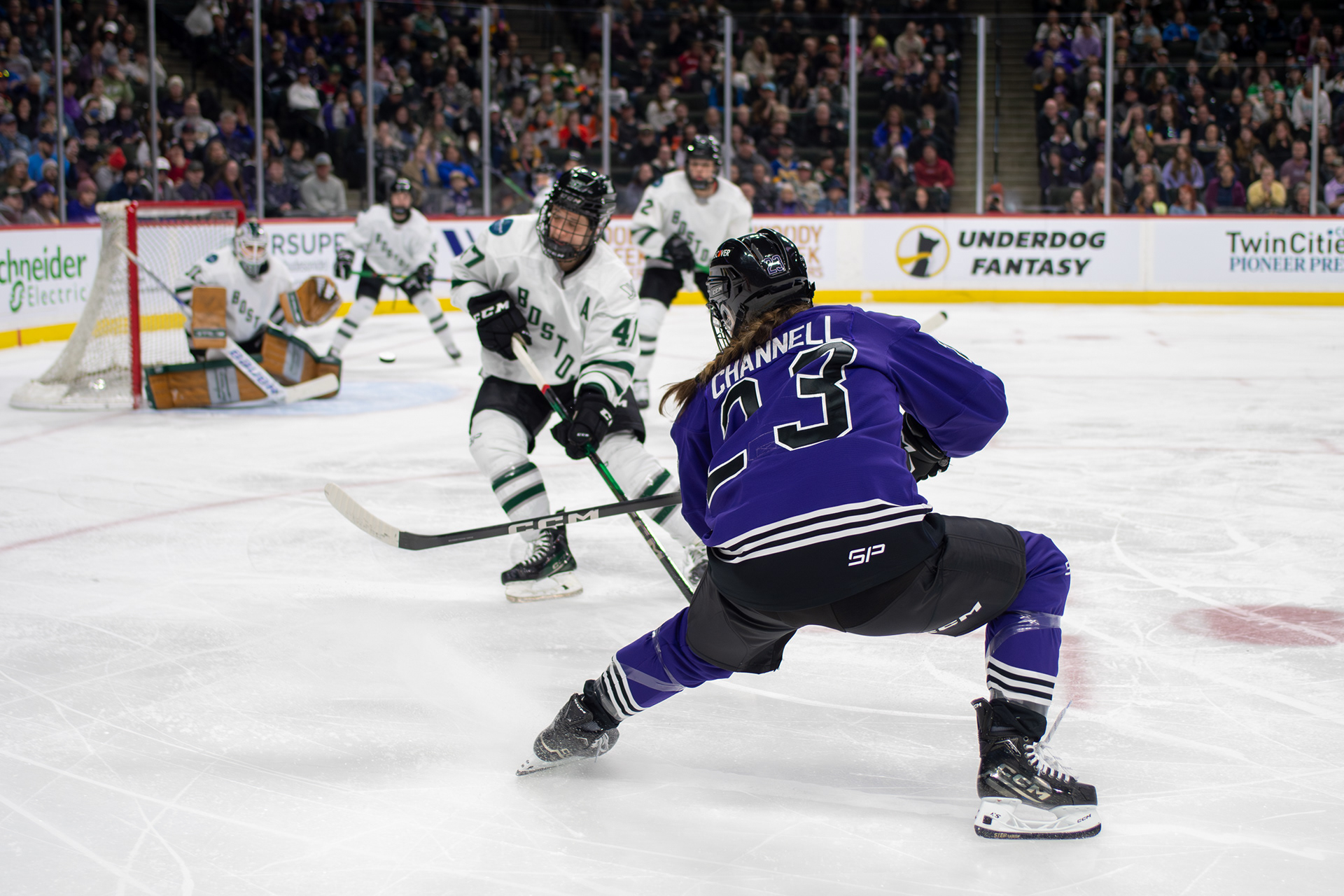 Profesional women's hockey player shooting a puck at the net in a purple jersey.