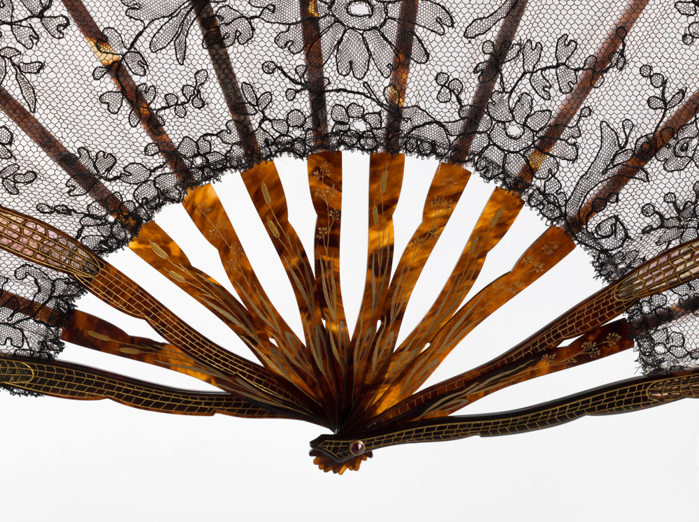 Eventail, composé de 12 brins. Feuille en dentelle de Chantilly noire à motif sur fond de gaze rose, monture en écaille jaspée, gravée et dorée, panache, contre-panache et 2 brins en forme d'aile de papillon en écaille repercée et appliquée sur un fond d'alliotis à reflets rose et vert, rivure en pierre rouge. 1895-1905. Galliera, musée de la Mode de la Ville de Paris. © Julien vidal / Roger-Viollet