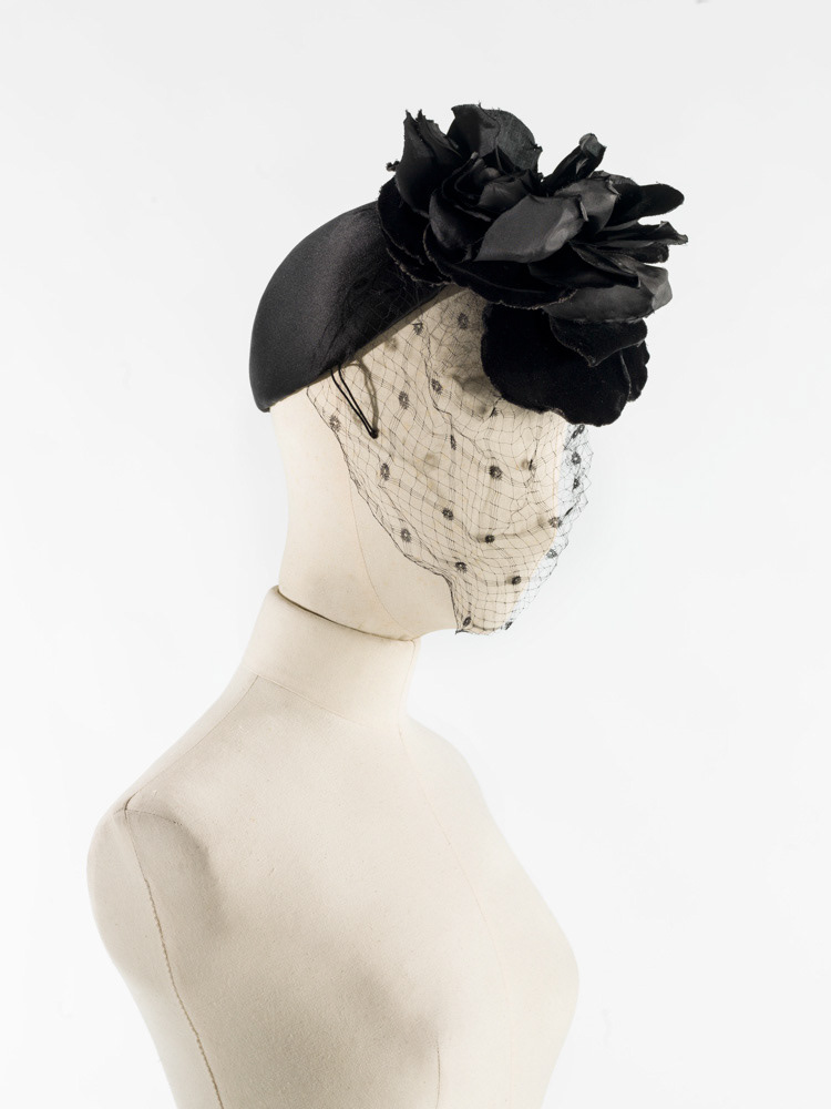 Cristobal Balenciaga (1895-1972). Calotte. Calotte de satin noir, montée sur sparterie, 2 pattes laitonnées, décor en velours et taffetas noir, voilette noire. 1960. Galliera, musée de la Mode de la Ville de Paris. © Julien vidal / Roger-Viollet