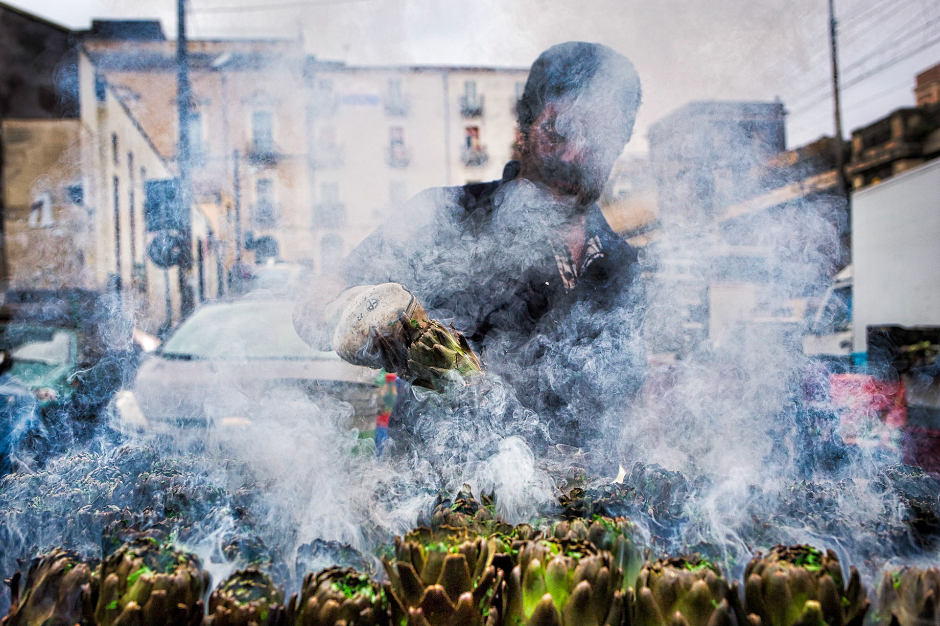 A man cooking artichokes in the streets of the Catania market.  It looks like a ghost among the flames of the underworld.