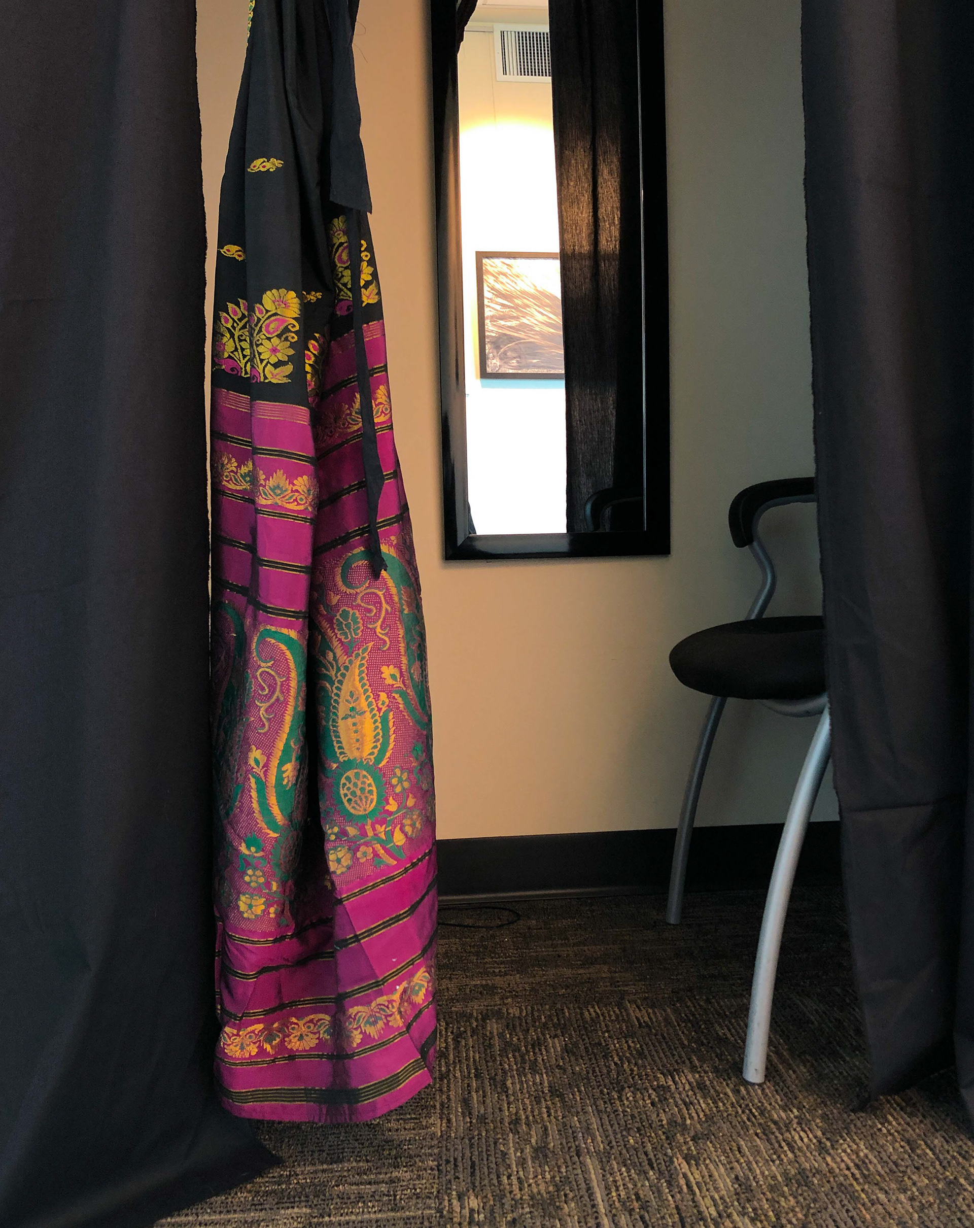 A sari acts as a doorway into the booth while a full-length mirror invites the viewer to consider the labour put into their own clothing.