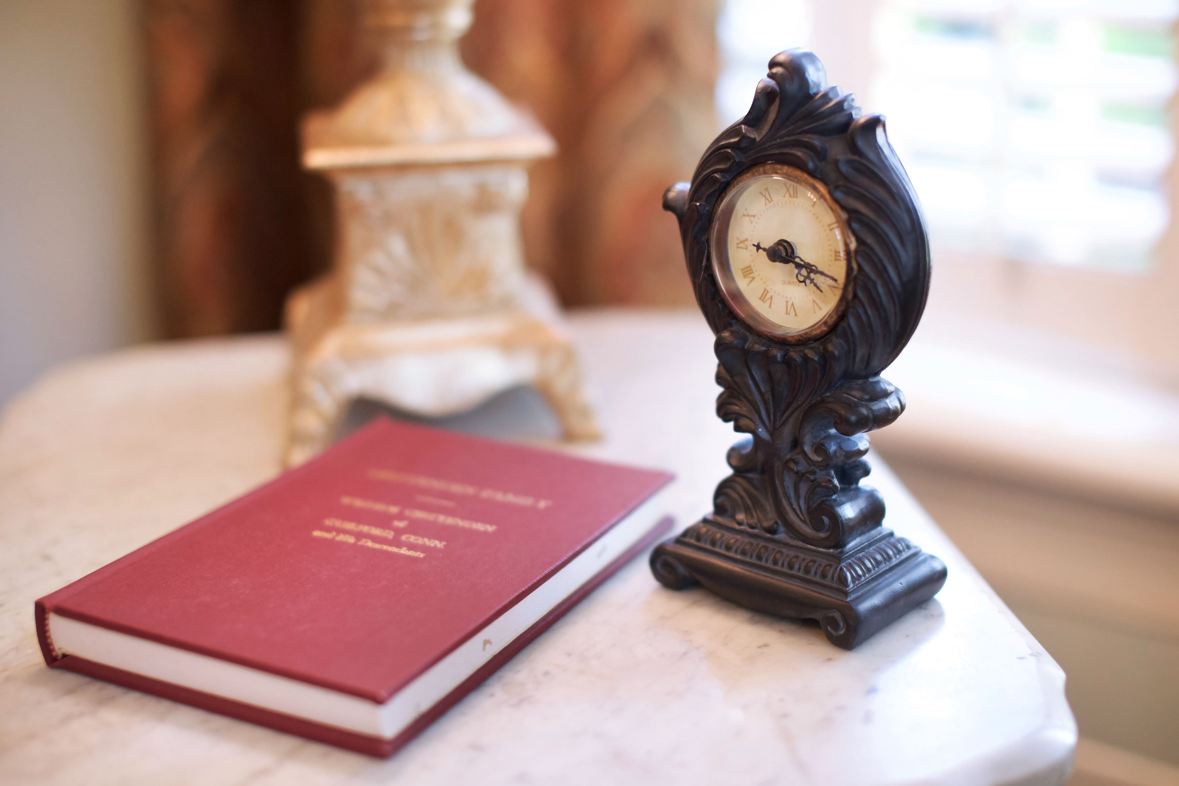 Shows a desk with a old clock and book.