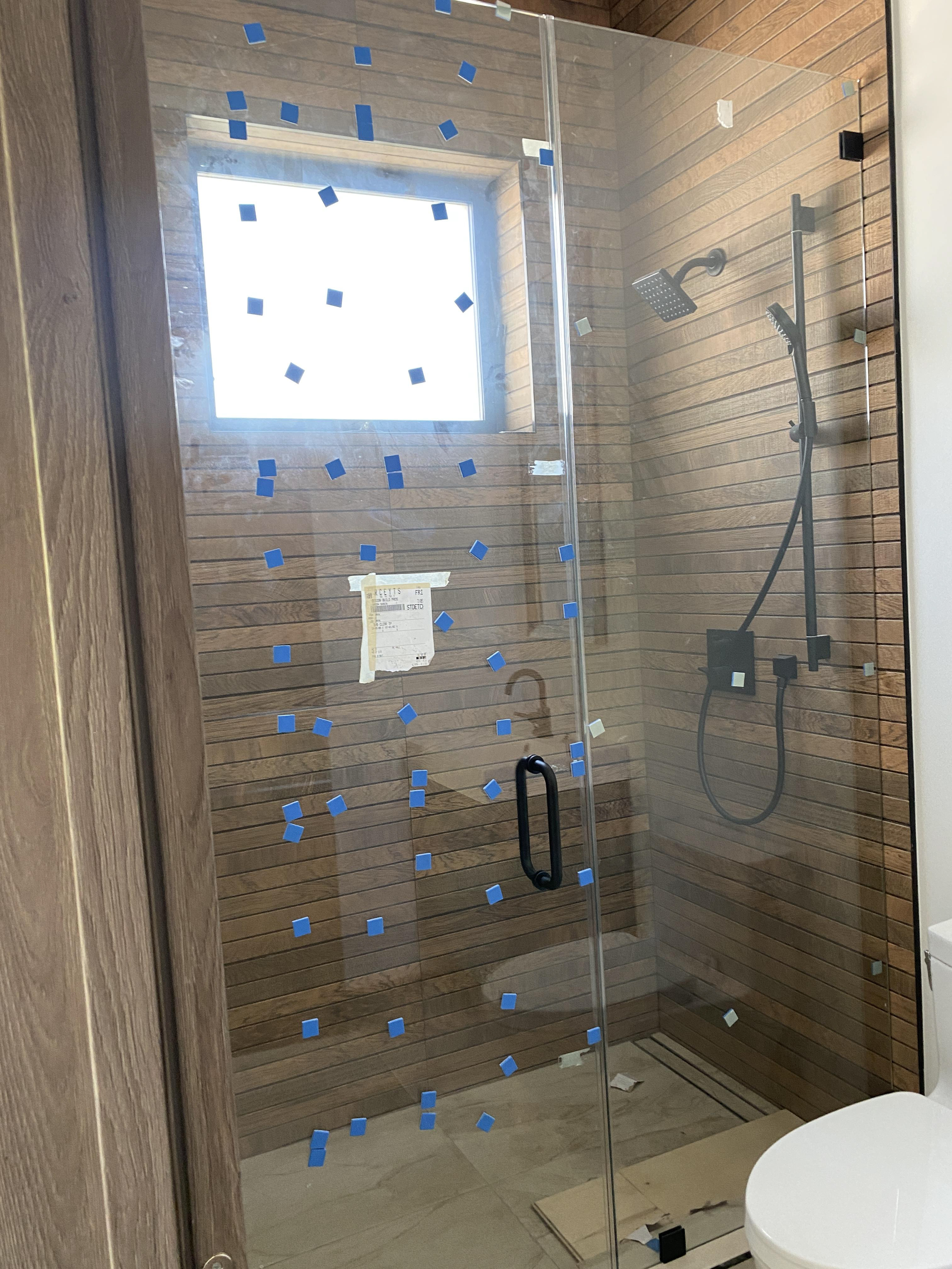Glass shower door installation in progress with protective tape on glass panels