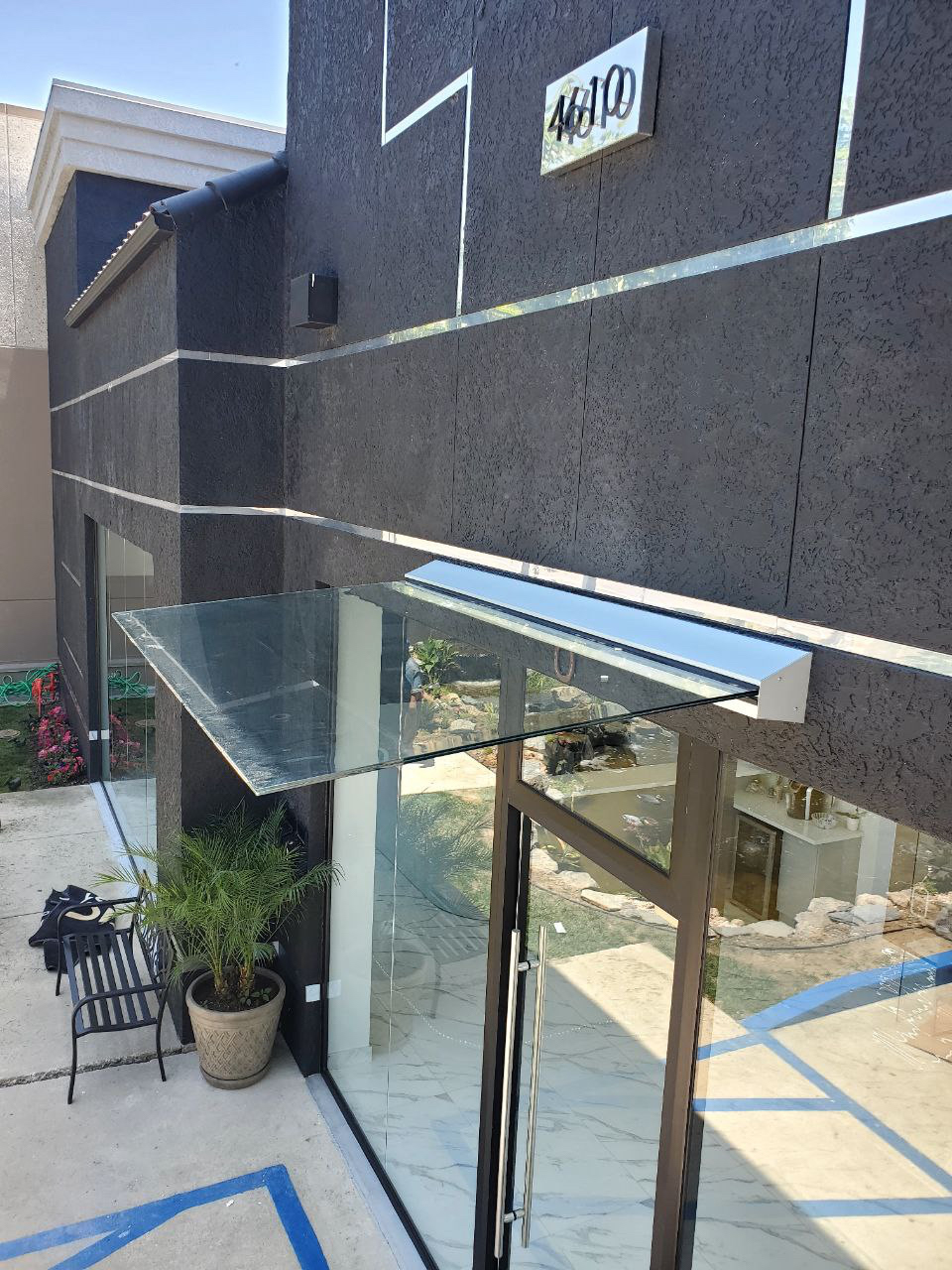 Custom glass entrance canopy with aluminum wall-mounted support system on a modern building.