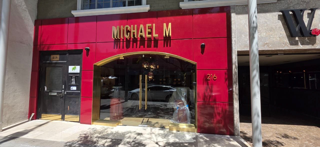 Commercial glass storefront with gold-finish double entrance doors and red aluminum composite panel facade installed by Design Build Pros.