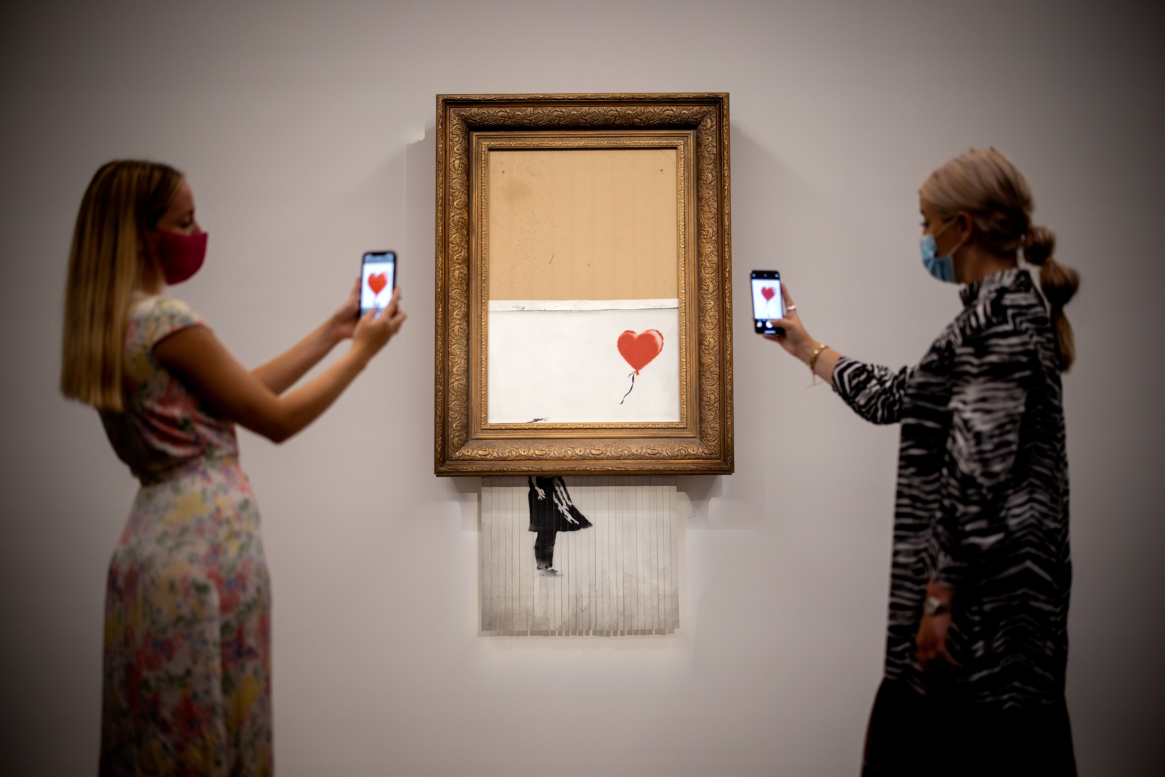 Assistants pose by an artwork titled Love is the Bin by British street artist Banksy during a photocall at Sothebys auction house in central London on September 3, 2021.