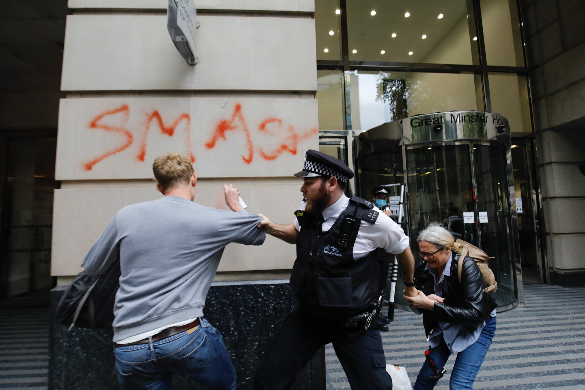 A police officer tries to stop an activist spraying graffiti on a wall