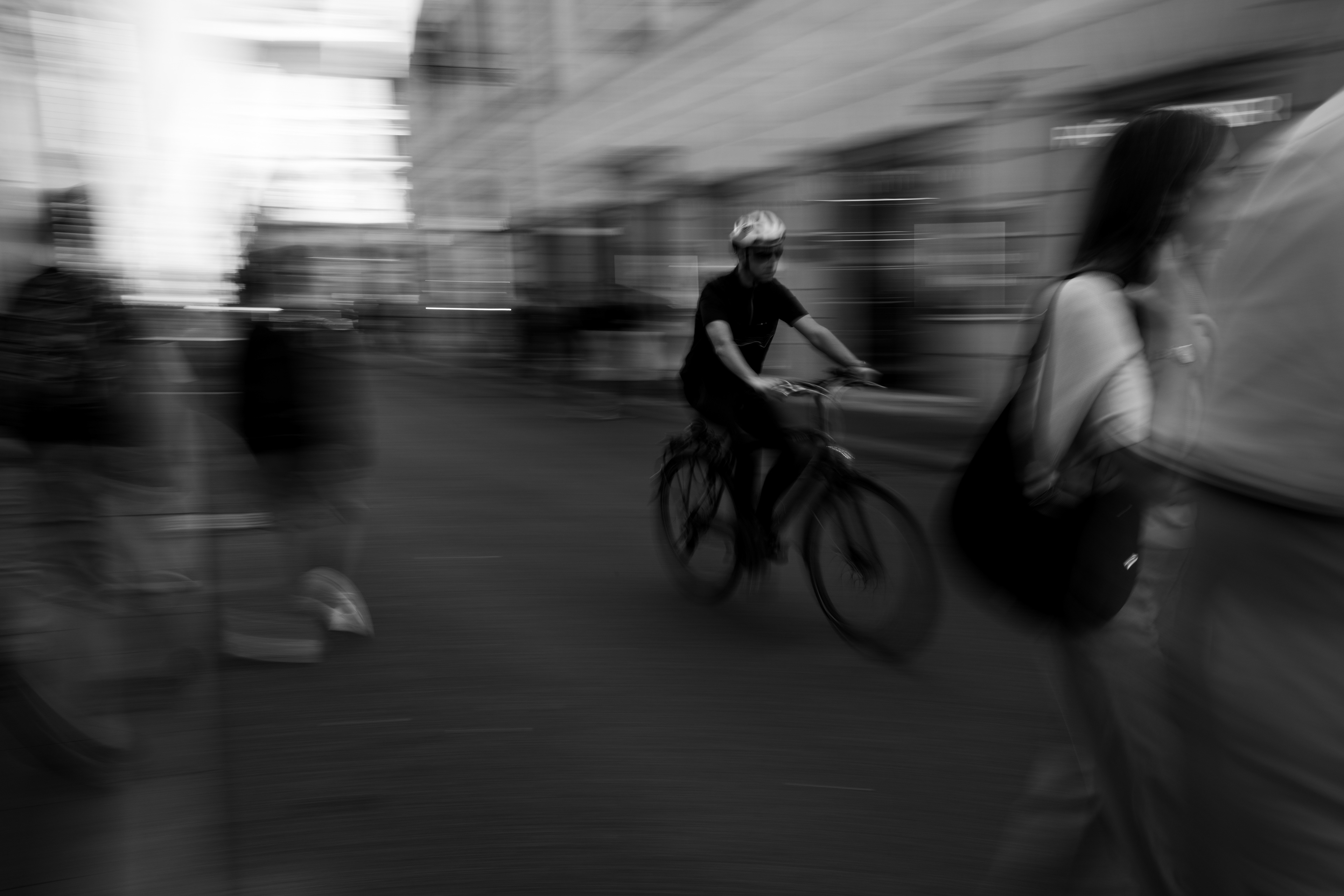 Lo spazio accelera: ciclista con casco tra scie di movimento e passanti sfocati in una via di Roma, zoom burst in bianco e nero, fotografia di Fabio Alimonti