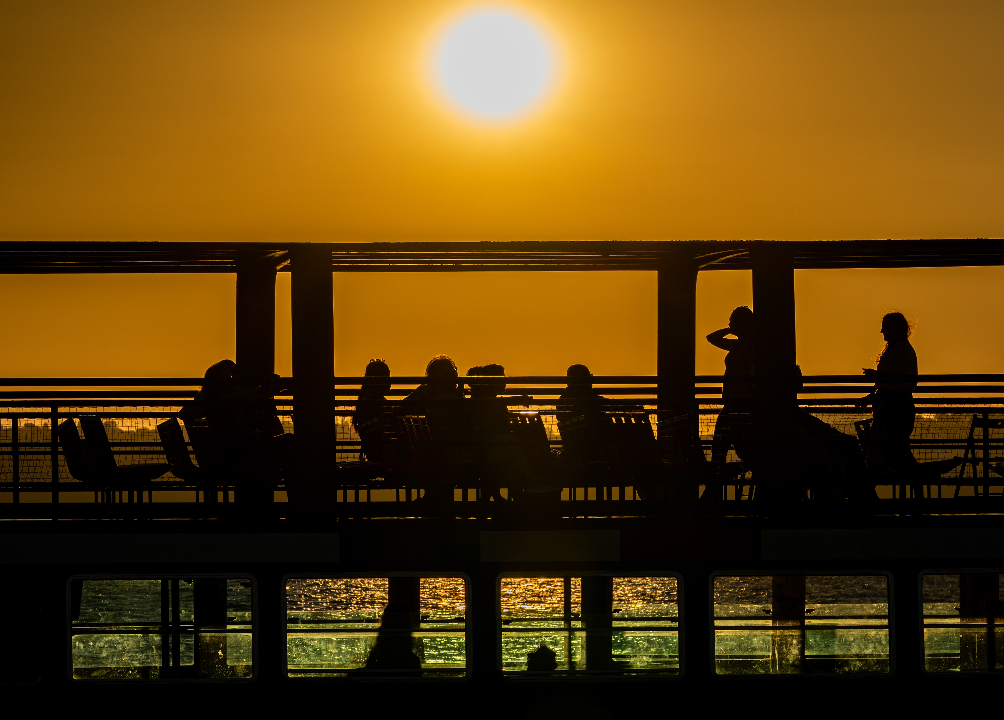 Passeggeri in controluce sul ponte del battello al tramonto sul lago di Bracciano, Anguillara Sabazia.