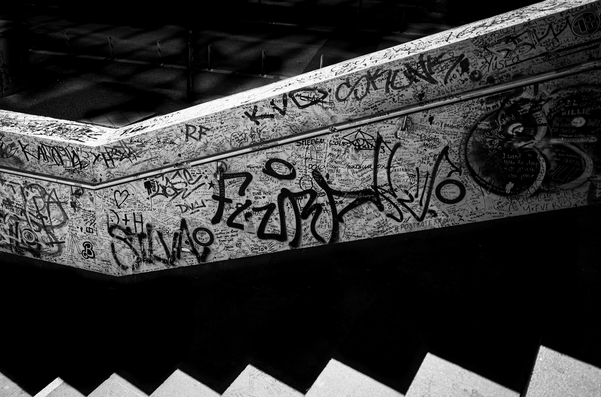 Mille firme – il parapetto di una scala a Berlino coperto di scritte e graffiti, tagliato in diagonale da luce e ombra. Fotografia in bianco e nero di Fabio Alimonti.
