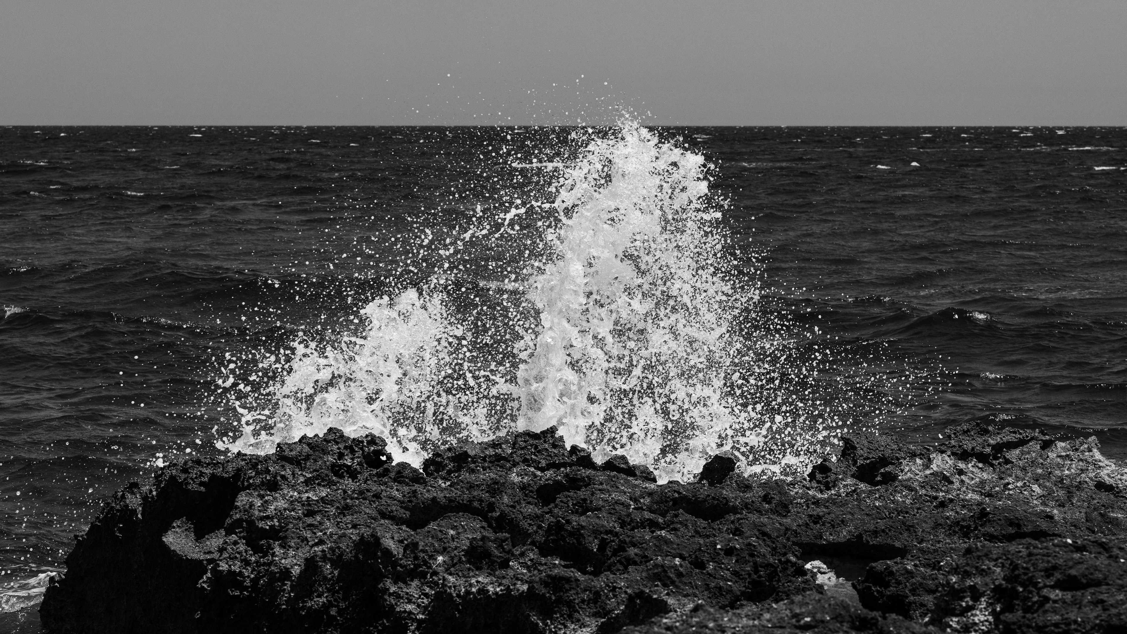 Effervescenza: onda che esplode in schiuma bianca sugli scogli, mare e orizzonte in bianco e nero, Cala Masciola, Puglia, fotografia di Fabio Alimonti