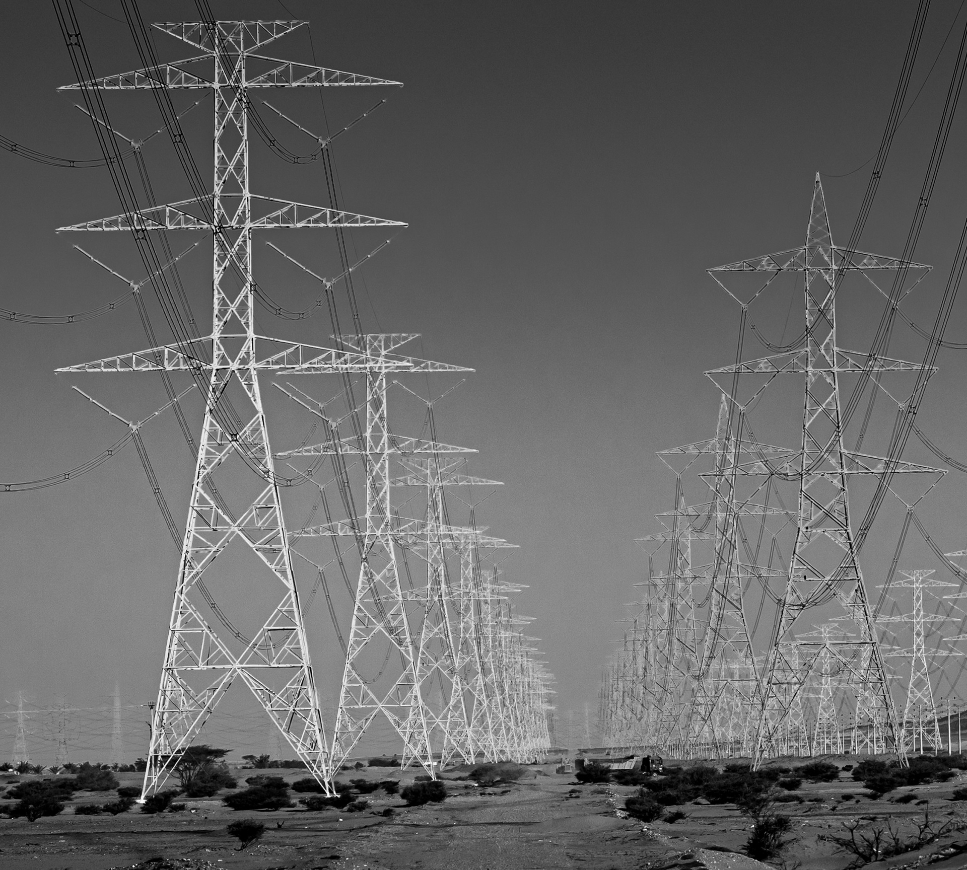 Tralicci dell'alta tensione in fila nel deserto dell'Arabia Saudita, in bianco e nero