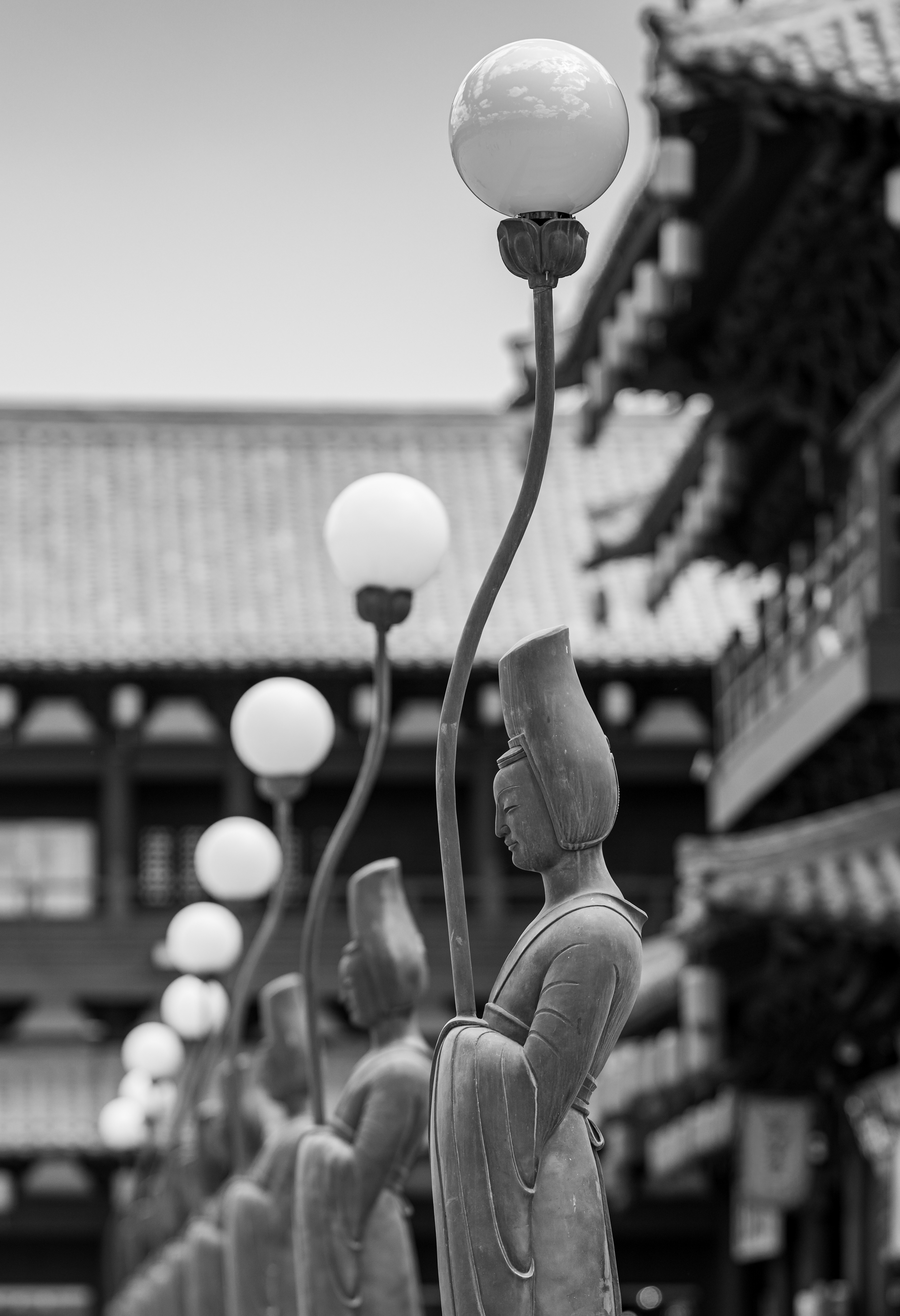 Il corteo – fila di statue in pietra sotto lampioni a fiore di loto nella città antica di Datong, Cina, fotografia in bianco e nero di Fabio Alimonti