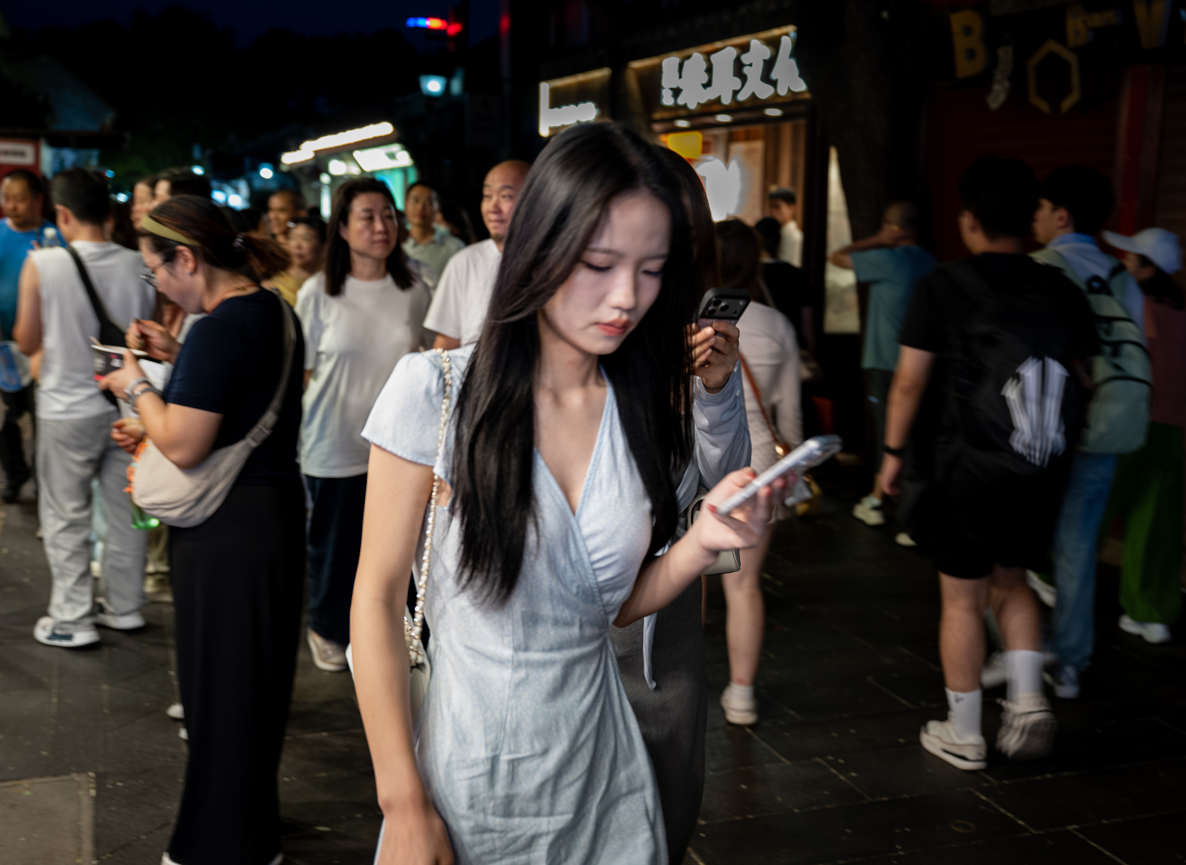 Sola tra tutti – una giovane donna guarda il telefono in una via affollata di sera, Datong, Cina