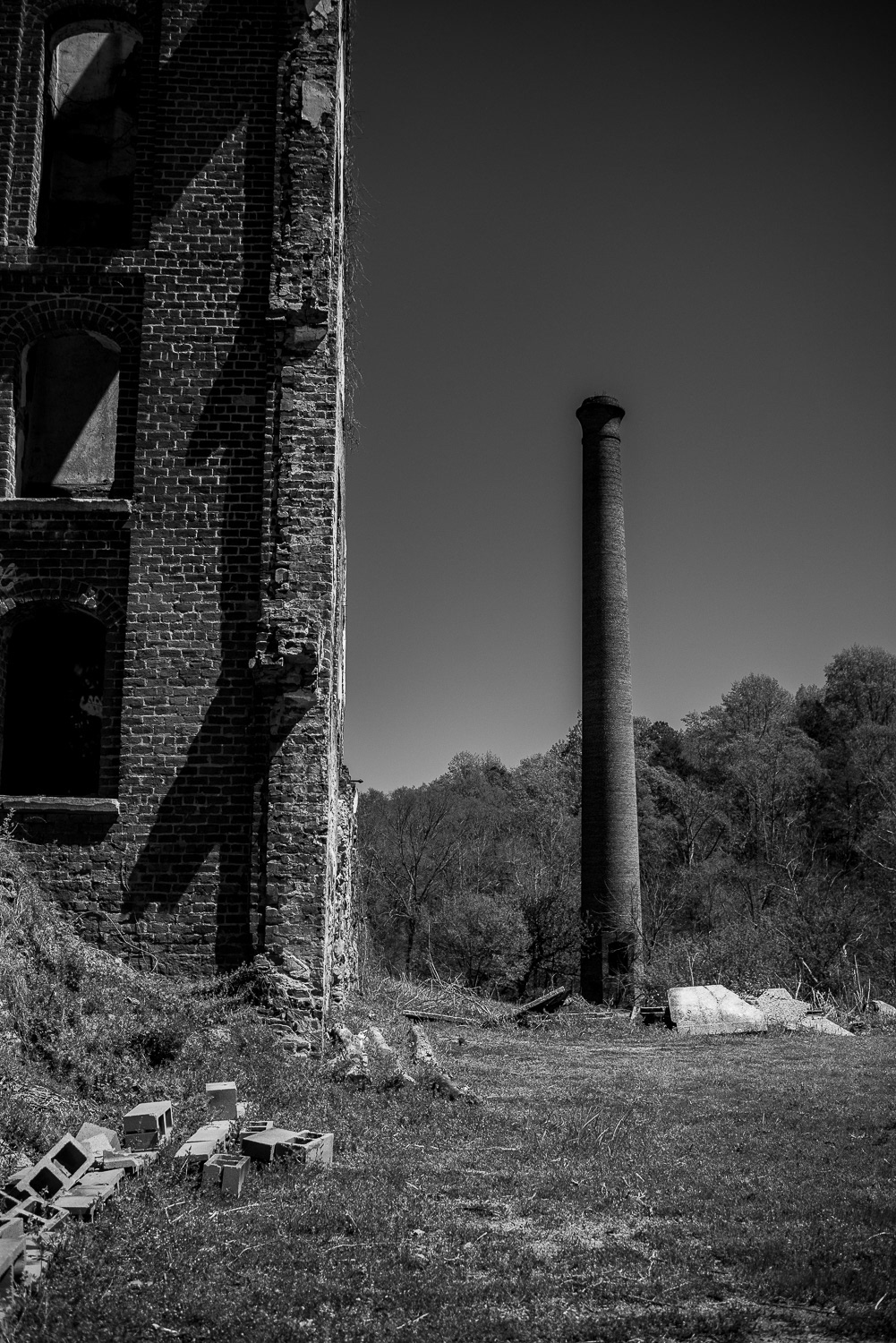 A black and white photograph showing a partial view of the Glendale Mill elevator shaft with a smaller silo visible in the background. Brick fragments rest in the foreground, framing the scene with quiet disrepair. Captured before the fire that destroyed the site, the image preserves a layered perspective of the mill's industrial past.