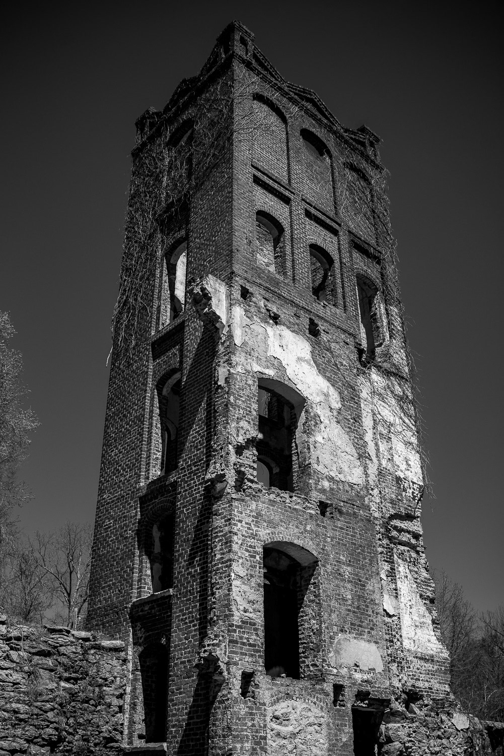 A black and white photograph of the elevator shaft at the former Glendale Mill in Spartanburg, South Carolina. The weathered brick structure stands alone in the aftermath of a fire, its vertical form a quiet remnant of a once-active textile mill.
