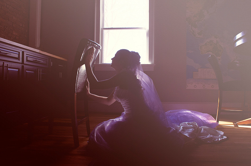 Artistic bridal portrait of a woman in silhouette kneeling beside a chair in natural window light, wearing a purple wedding gown, photographed indoors in Clemson, South Carolina.