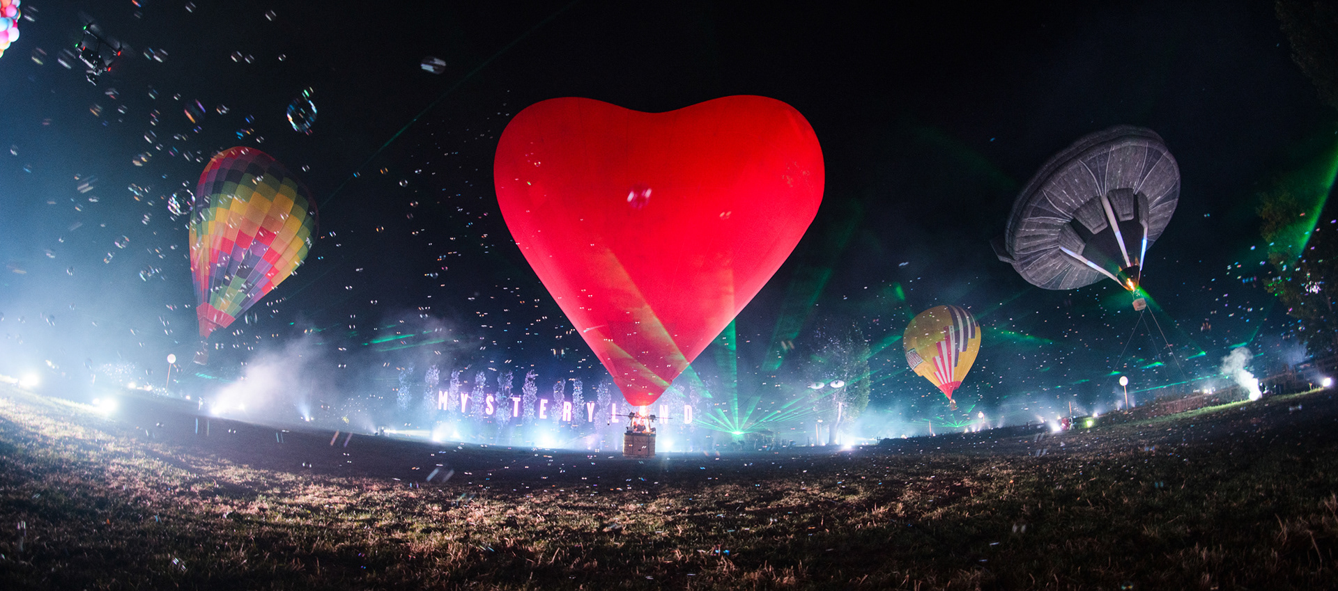 Night scene of a festival with multiple hot air balloons and lights and lasers.