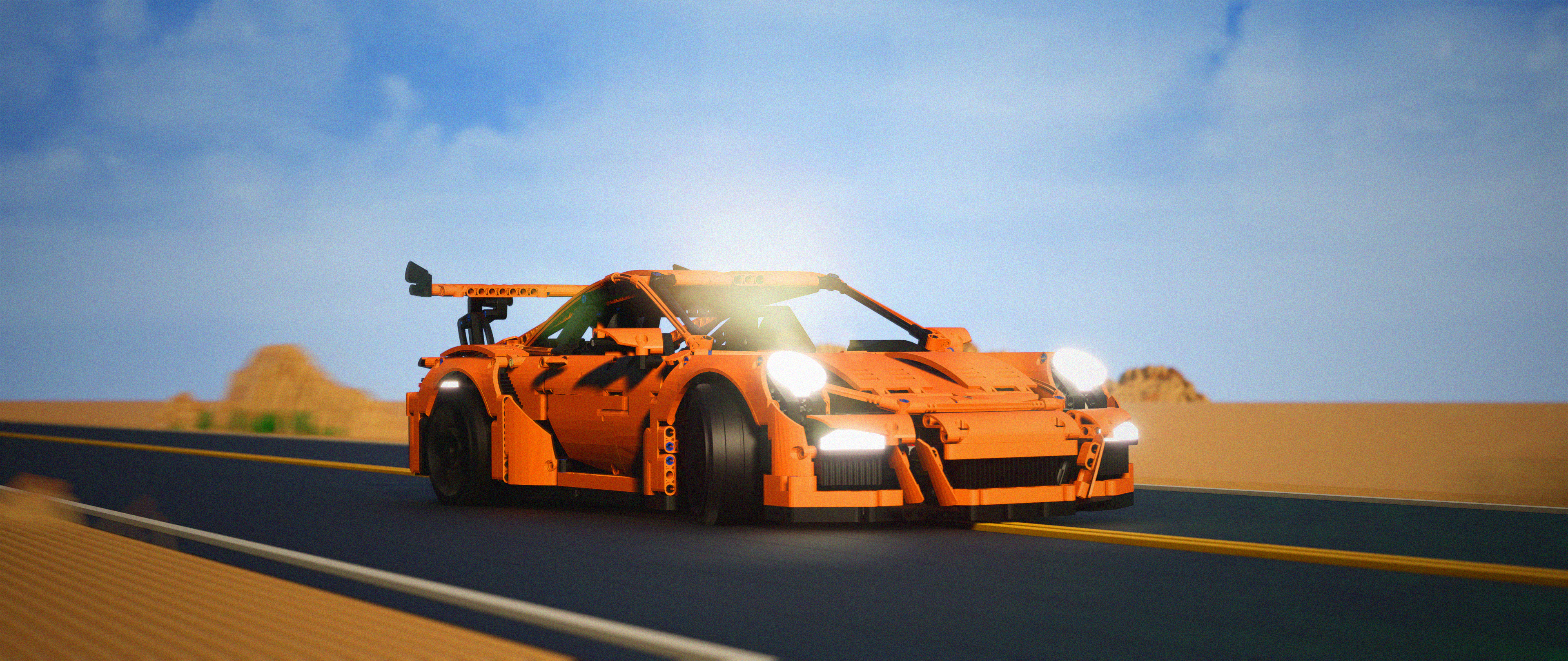 3D visualization of a orange Lego Technic sports car model on a desert road with headlights on.