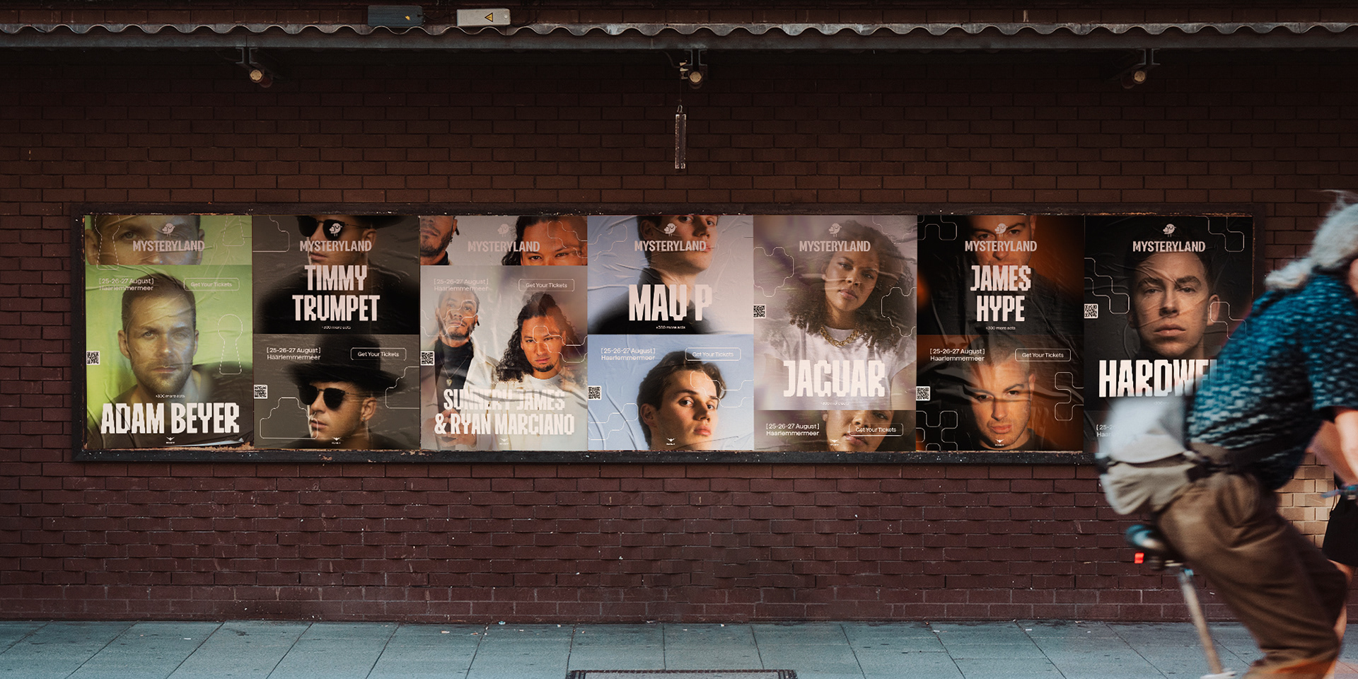 Billboard with Mysteryland event posters displaying dj’s and artists on a brick wall.