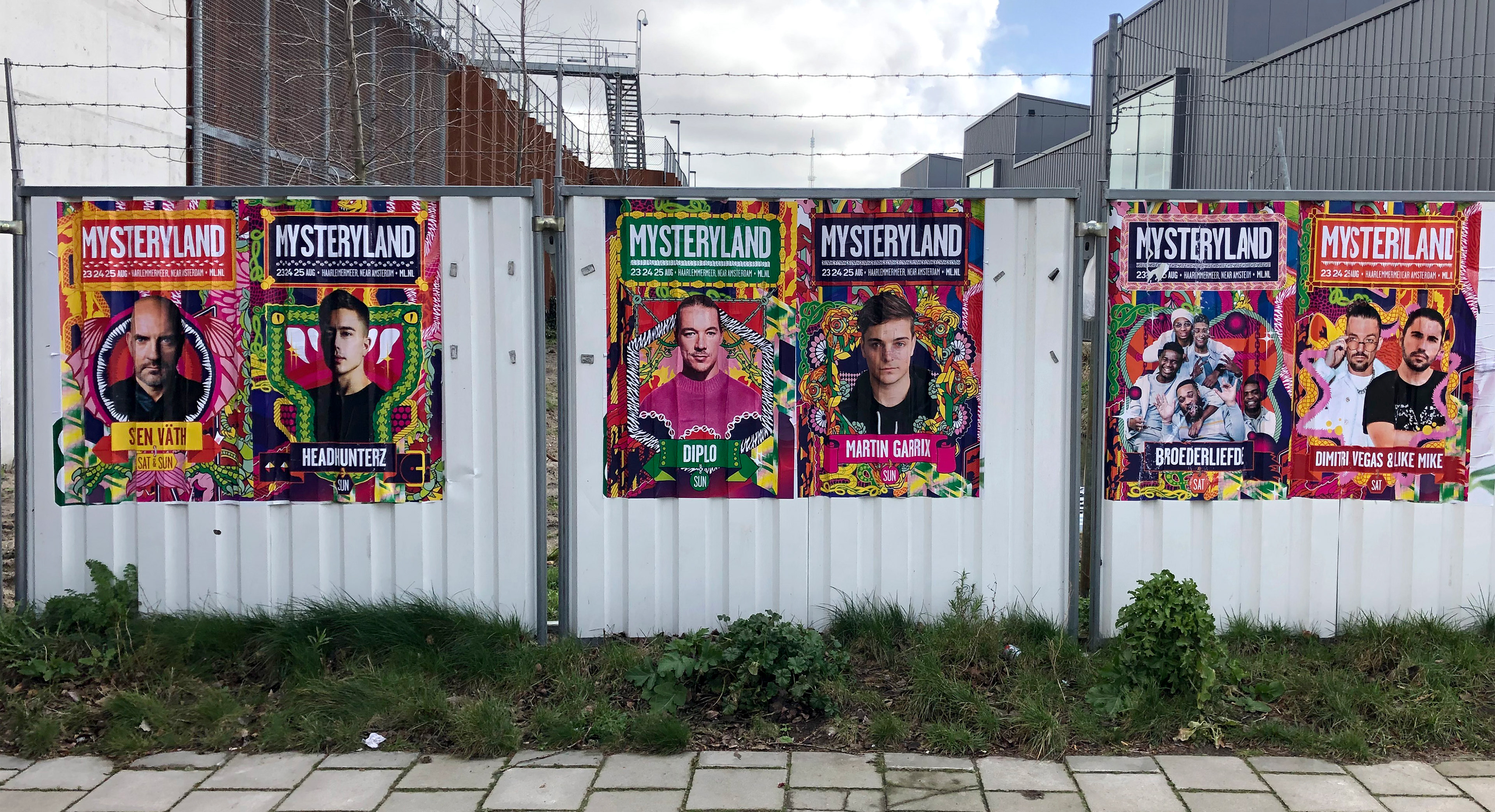 Posters on a fence promoting the Mysteryland music festival with colorful artwork.