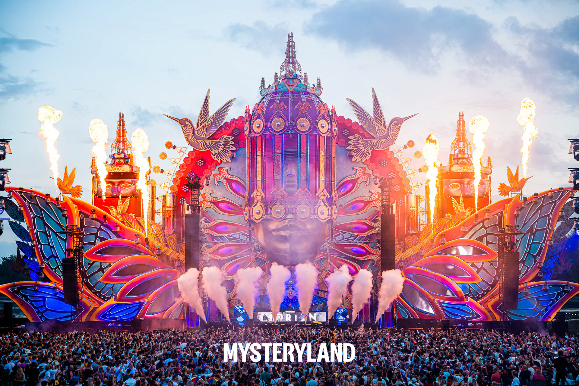 A vibrant festival stage with fire effects and a large crowd at Mysteryland.