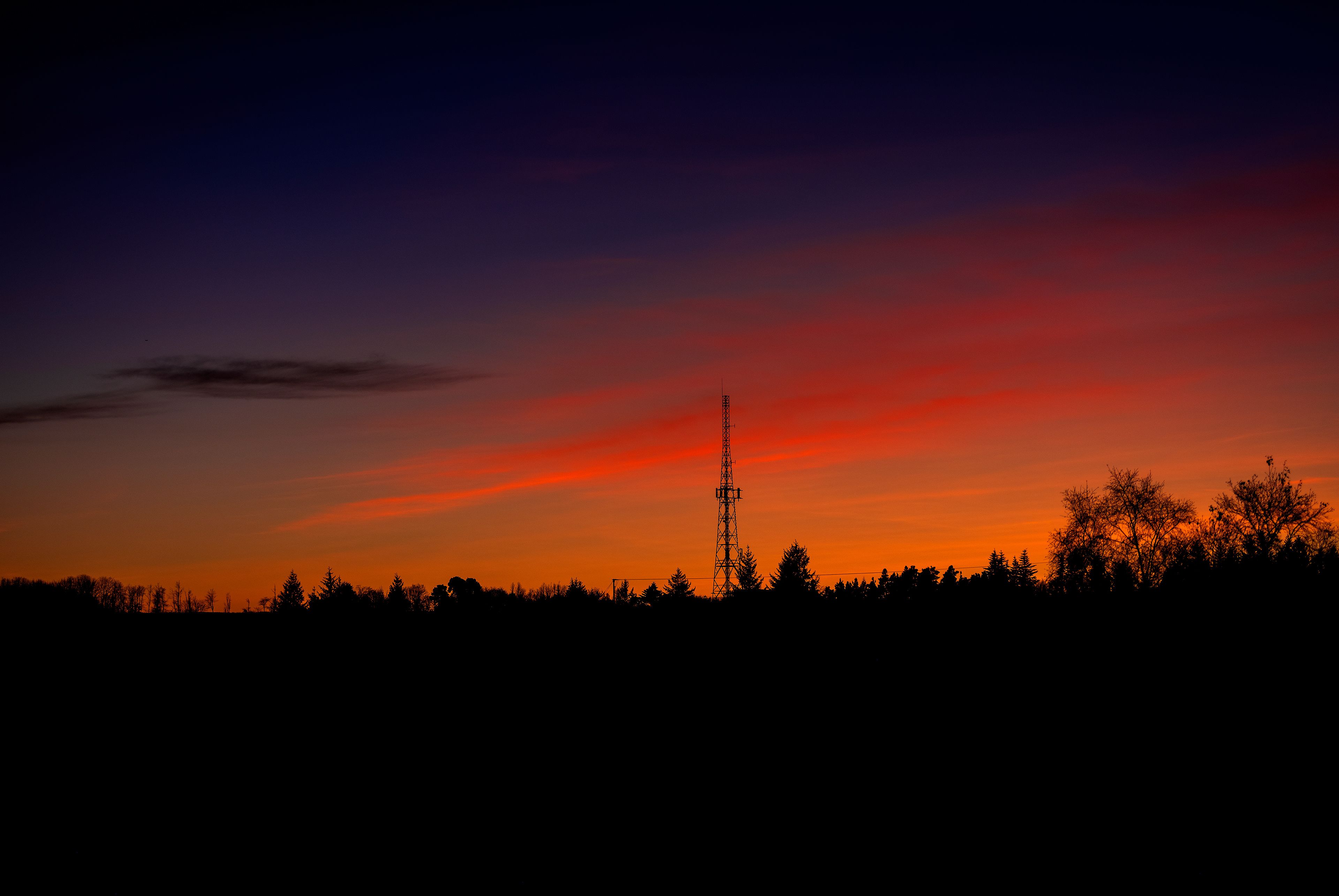 Sunset photograph of Penicuik's old TV mast in the distance, with a silhouette of trees agains the red sunset 