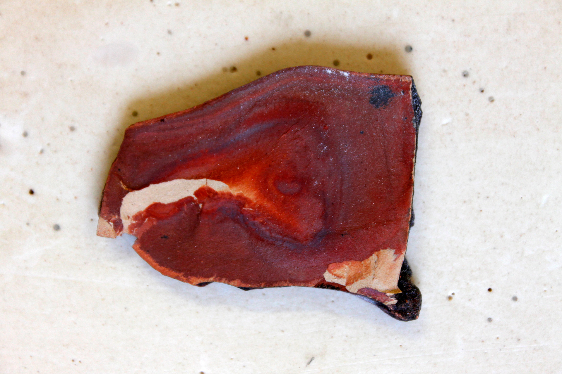 This fired piece of slate is from 53°21′32″N , 001°49′55″W. Slate is formed from compacted clay. The reason for the areas of white is that a layer of pale kaolin like clay was sedimented and compacted into the piece and through the firing process revealed.