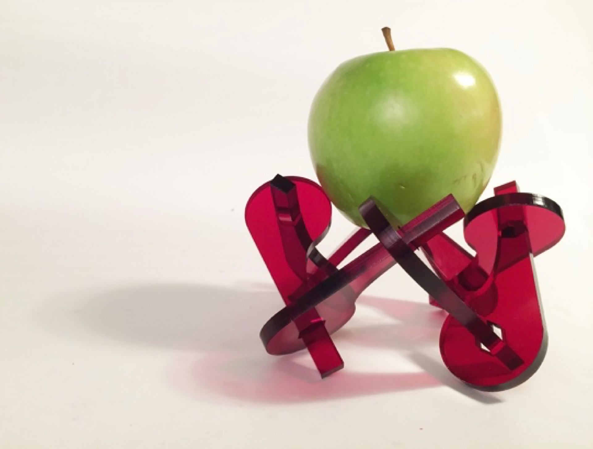 an apple sitting on a laser cut acrylic stand