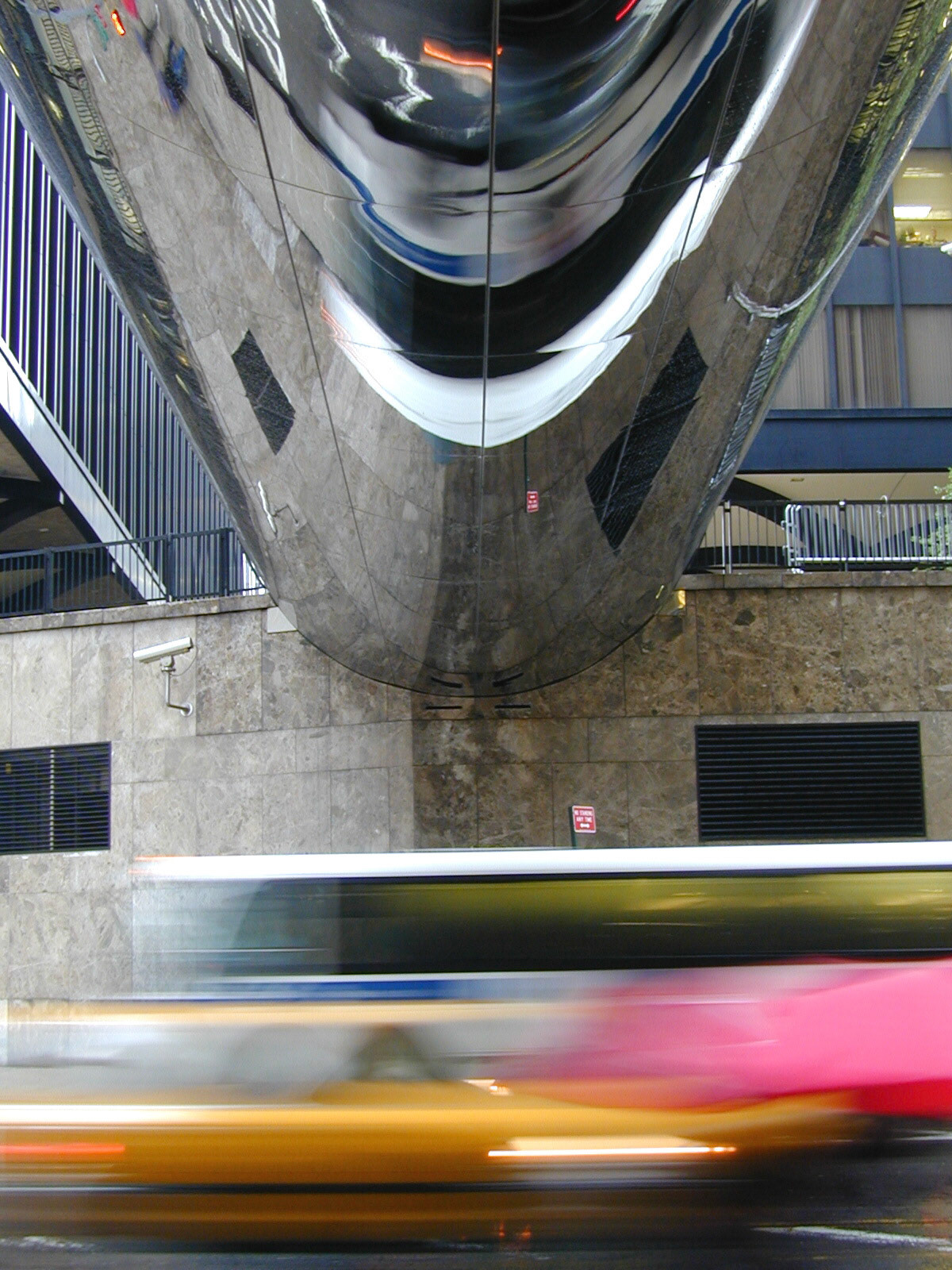 woman walking past with a pink umbrella in the rain under the chrome underpass to 7 world trade center