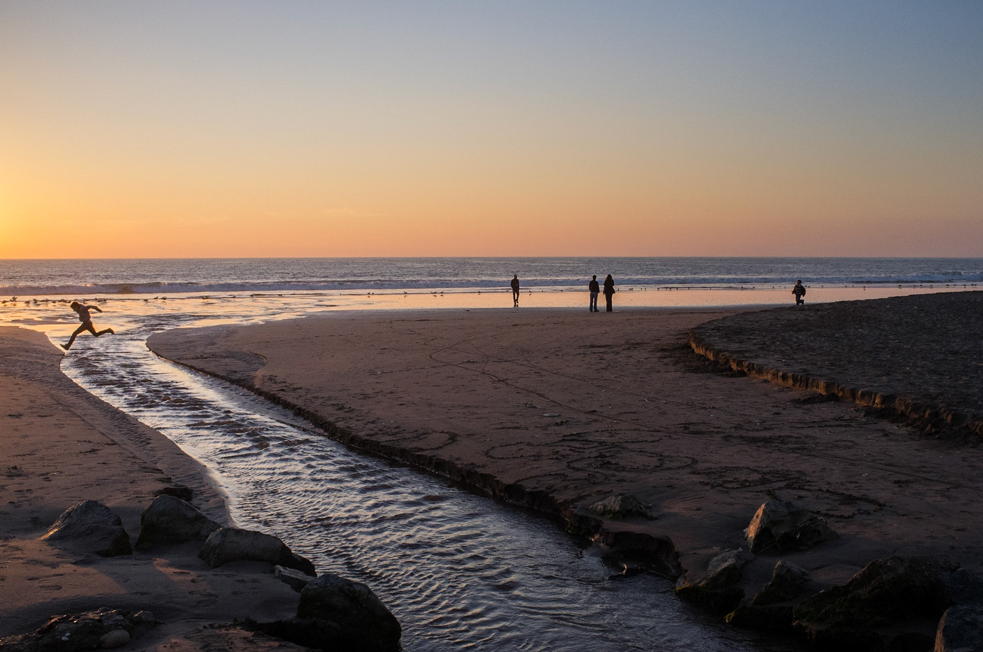 A boy jumps over a stream that drains into the Pacific.