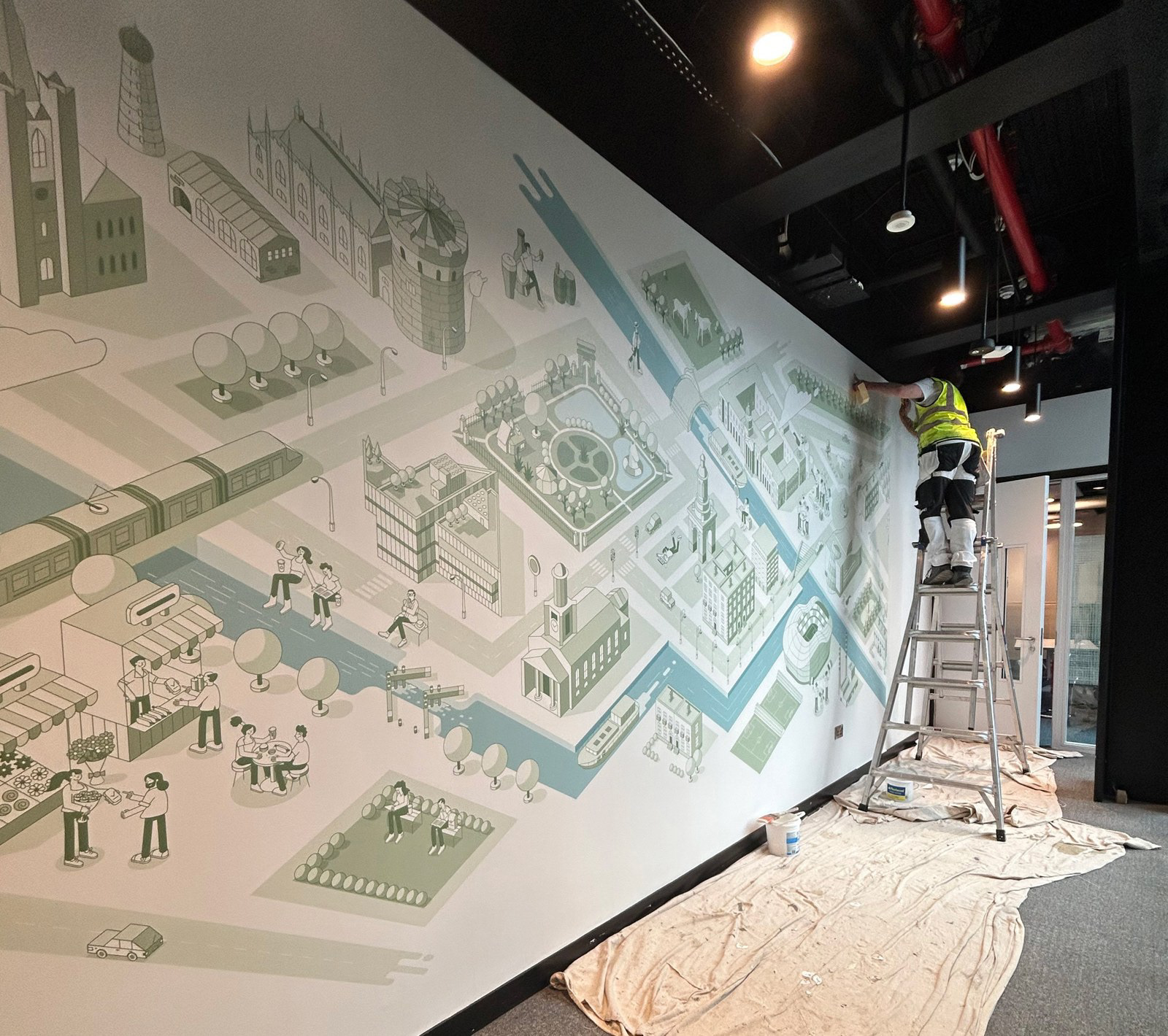 Installer on a ladder painting the isometric Dublin city map mural on an office wall