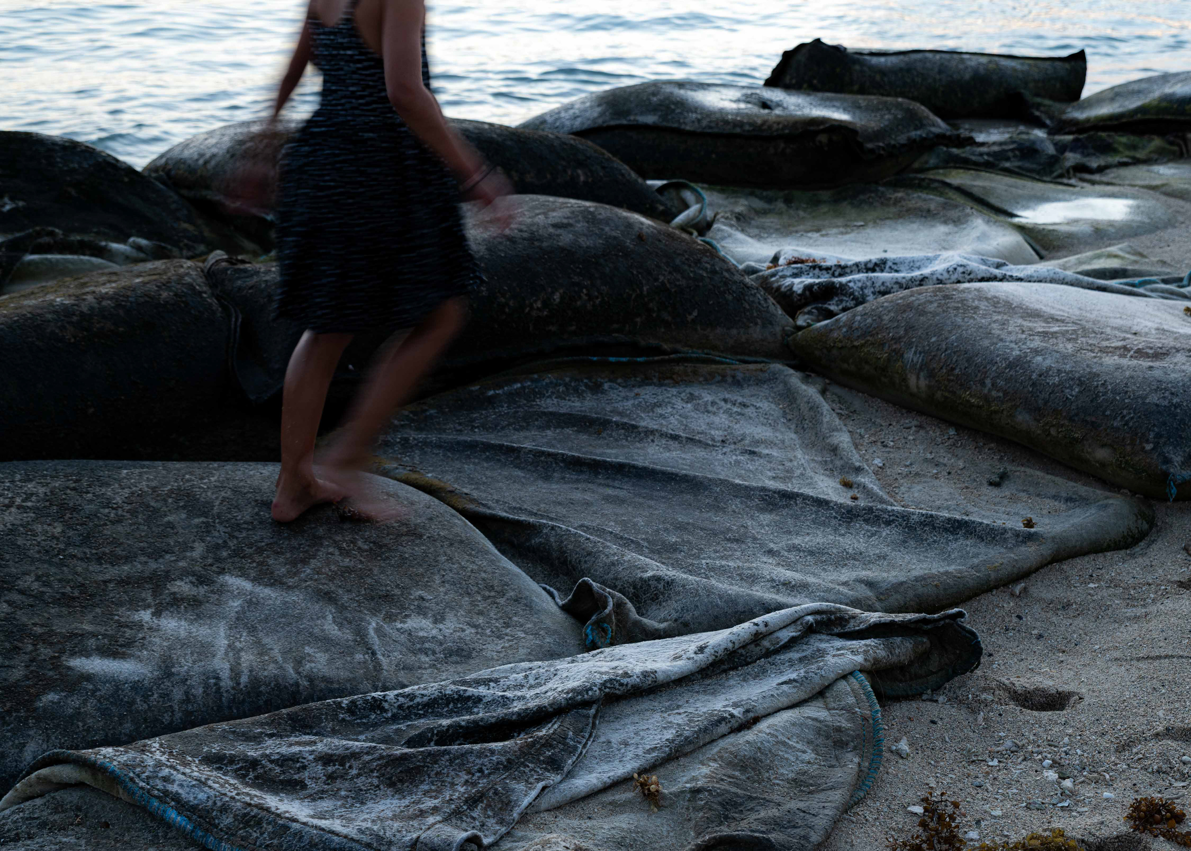 A young girl playing on the sand bags of La Preneuse public beach. The sand bags have been intalled to allegedly mitigate erosion. As a kid I used to run on wet sand and play on the dark volcanic rocks. Now kids run on sand bags, they laugh, they don't realise. It's not that they don't care, they're just kids...