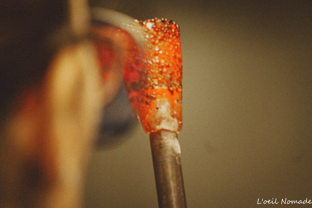 Photographie d'artisanat d'art : vue subjective du travail du verre en fusion sur canne, immersion dans le quotidien et la technicité d'une souffleuse de verre.