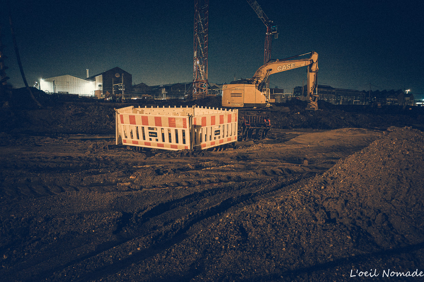Photographie de chantier réelle Le Havre, détails de traces de pneus dans la boue et texture de terre sous éclairage nocturne.