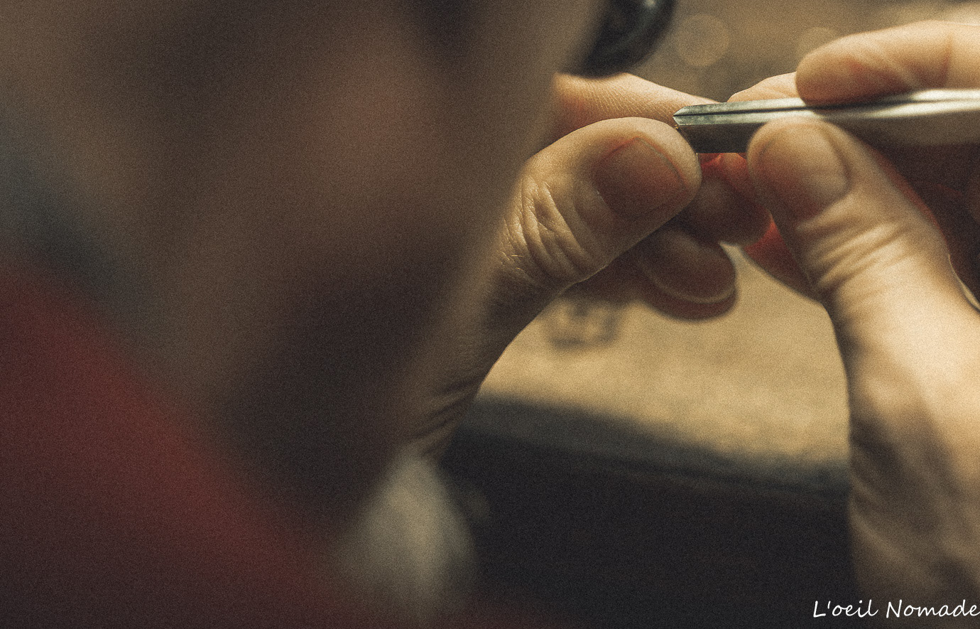 Mains de l'horloger manipulant une pièce minuscule avec un outil de précision, focus sur le geste artisanal.
