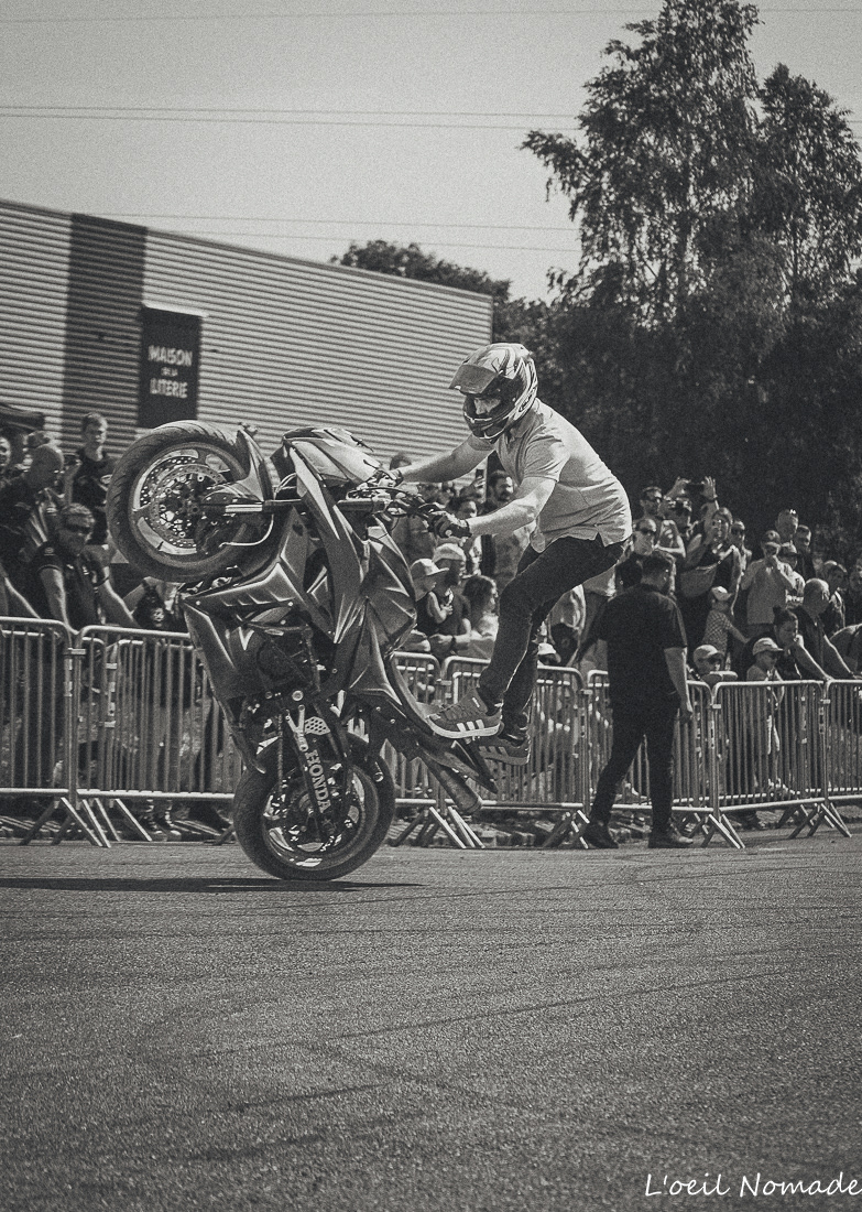 Pilote de stunt moto effectuant une figure technique sous le regard des spectateurs.