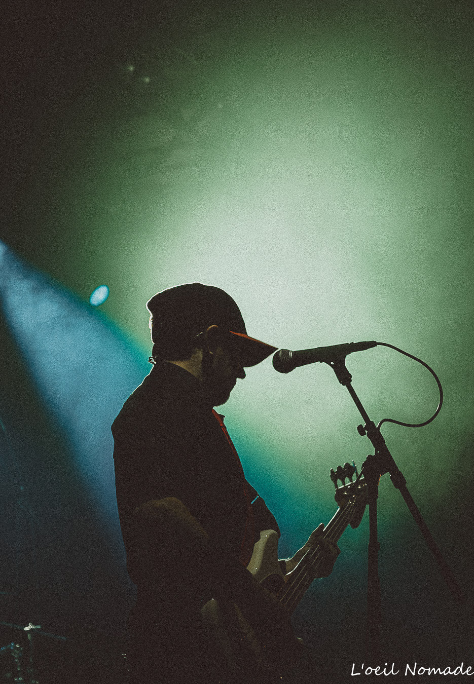 Photographie de concert au Havre : ombre et lumière sur un bassiste en silhouette sous un projecteur, illustrant la force du contraste en reportage événementiel.