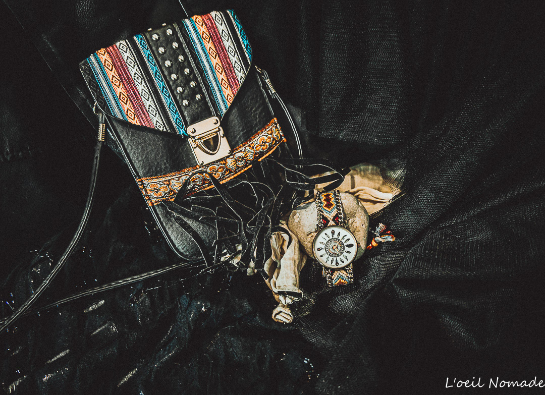 Packshot créatif : sac en cuir noir et montre style amérindien mis en scène sur un tissu sombre pour un contraste de matières élégant.