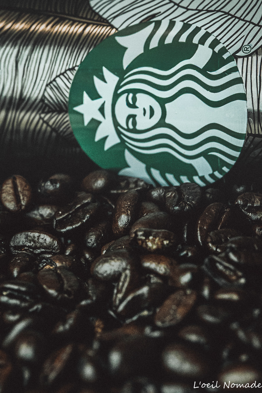 Photographie de commande : gobelet Starbucks personnalisé entouré de grains de café, éclairage tamisé pour un aspect haut de gamme.