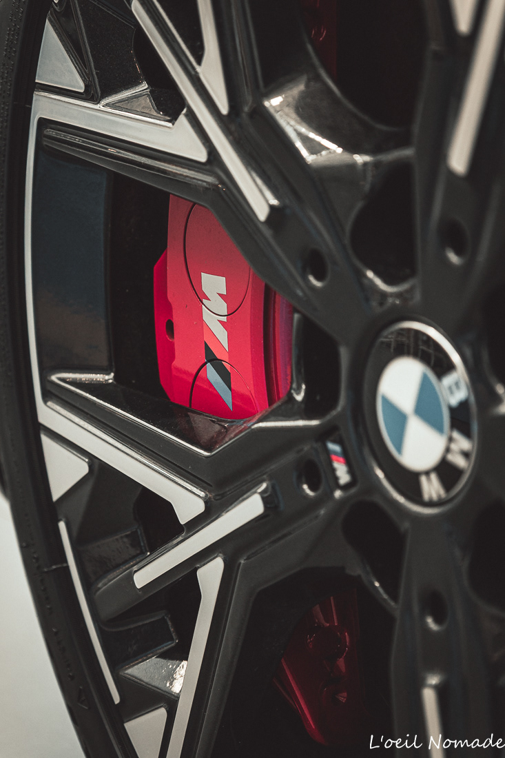 Détail technique jante automobile BMW avec logo M et étrier de frein rouge, reportage photo Groupe BMS Le Havre, style Dark Muted.
