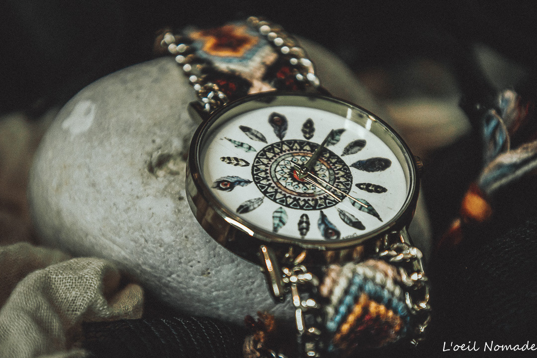 Photographie de produit : montre artisanale au cadran orné de plumes, posée sur un galet brut pour un rendu de texture naturel.