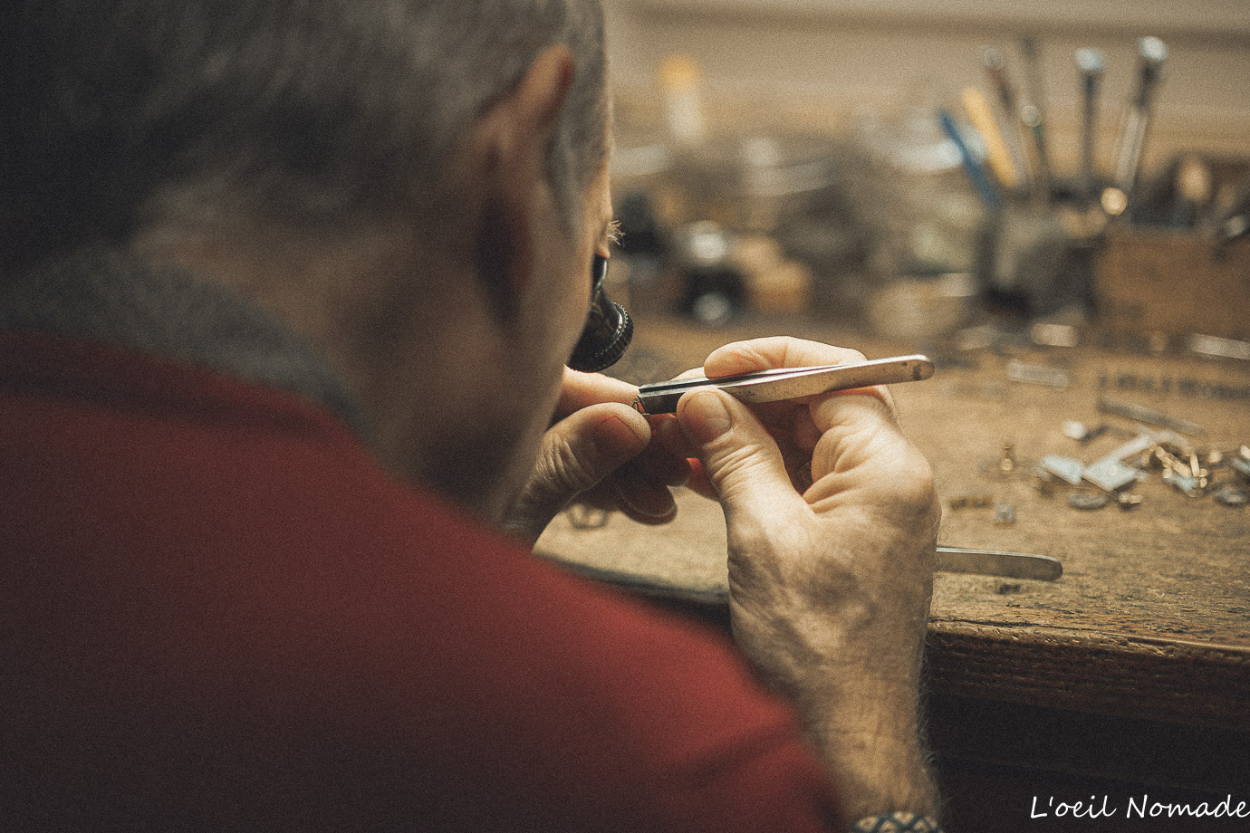 Artisan horloger au Havre concentré sur la réparation d'un mouvement, vue de profil en atelier.
