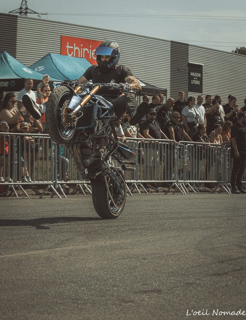 Pilote réalisant une roue arrière devant les spectateurs lors d'une démonstration de stunt moto.