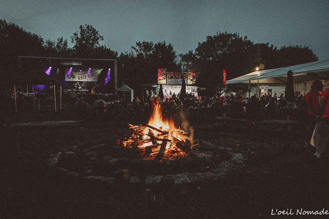 Reportage événementiel nocturne : un grand feu de camp éclairant une foule en arrière-plan, capturant la chaleur et la lumière naturelle lors d'un festival.